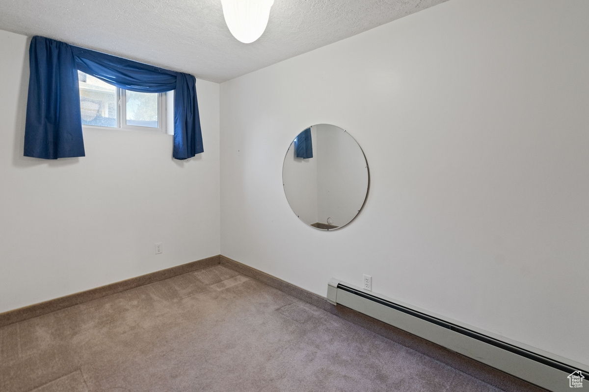 Unfurnished room with light colored carpet, a baseboard radiator, and a textured ceiling