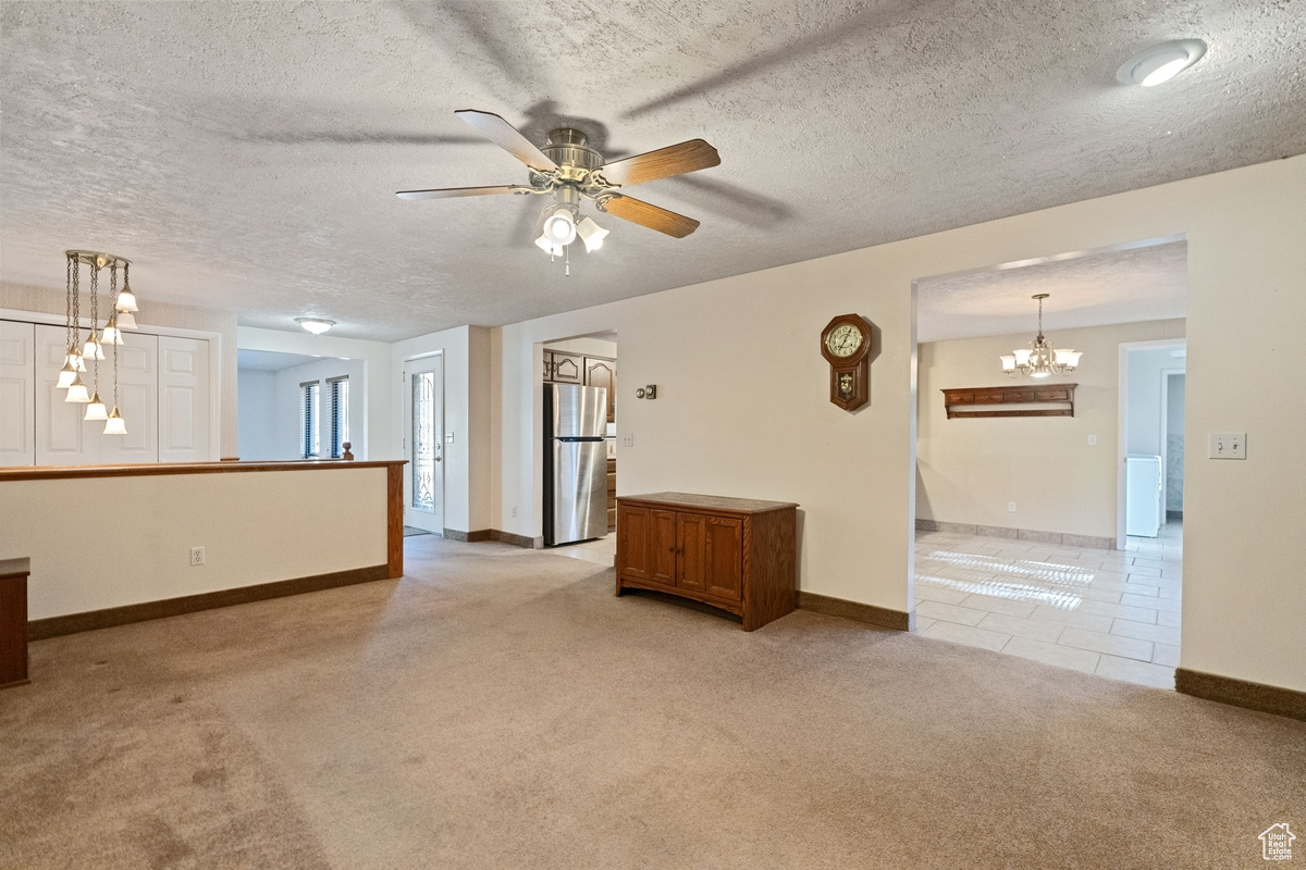 Unfurnished room with a textured ceiling, ceiling fan with notable chandelier, and light colored carpet