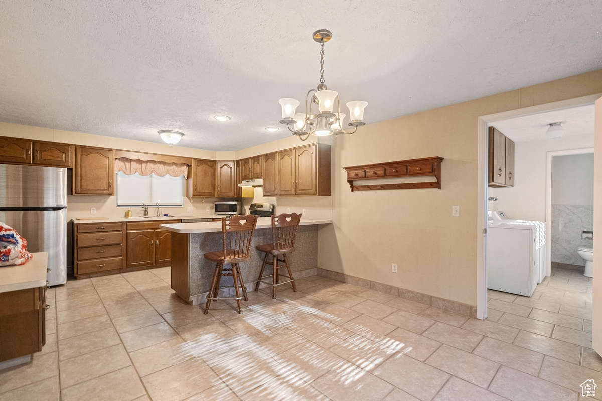 Kitchen featuring appliances with stainless steel finishes, kitchen peninsula, a kitchen bar, decorative light fixtures, and a notable chandelier