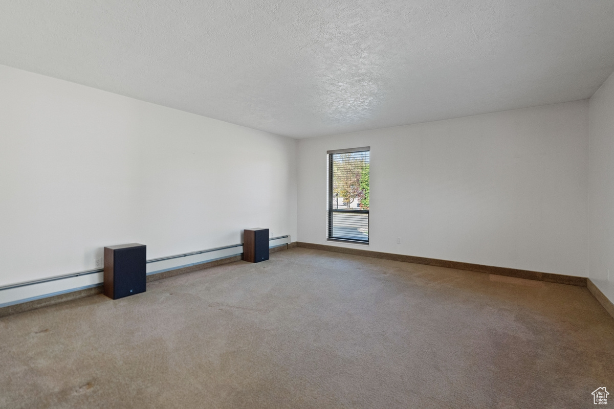 Empty room with a textured ceiling, a baseboard heating unit, and light colored carpet