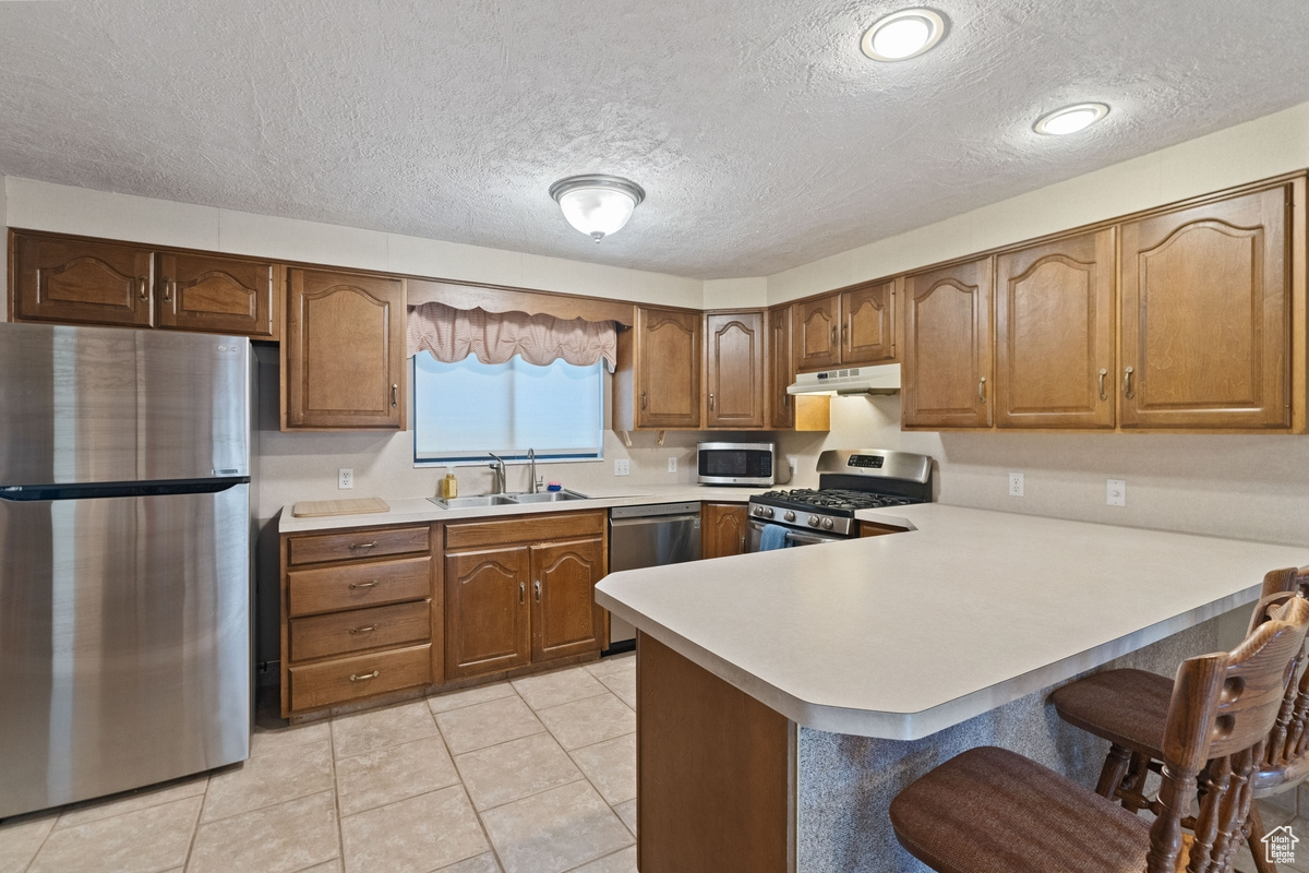 Kitchen featuring a textured ceiling, light tile patterned flooring, sink, kitchen peninsula, and appliances with stainless steel finishes