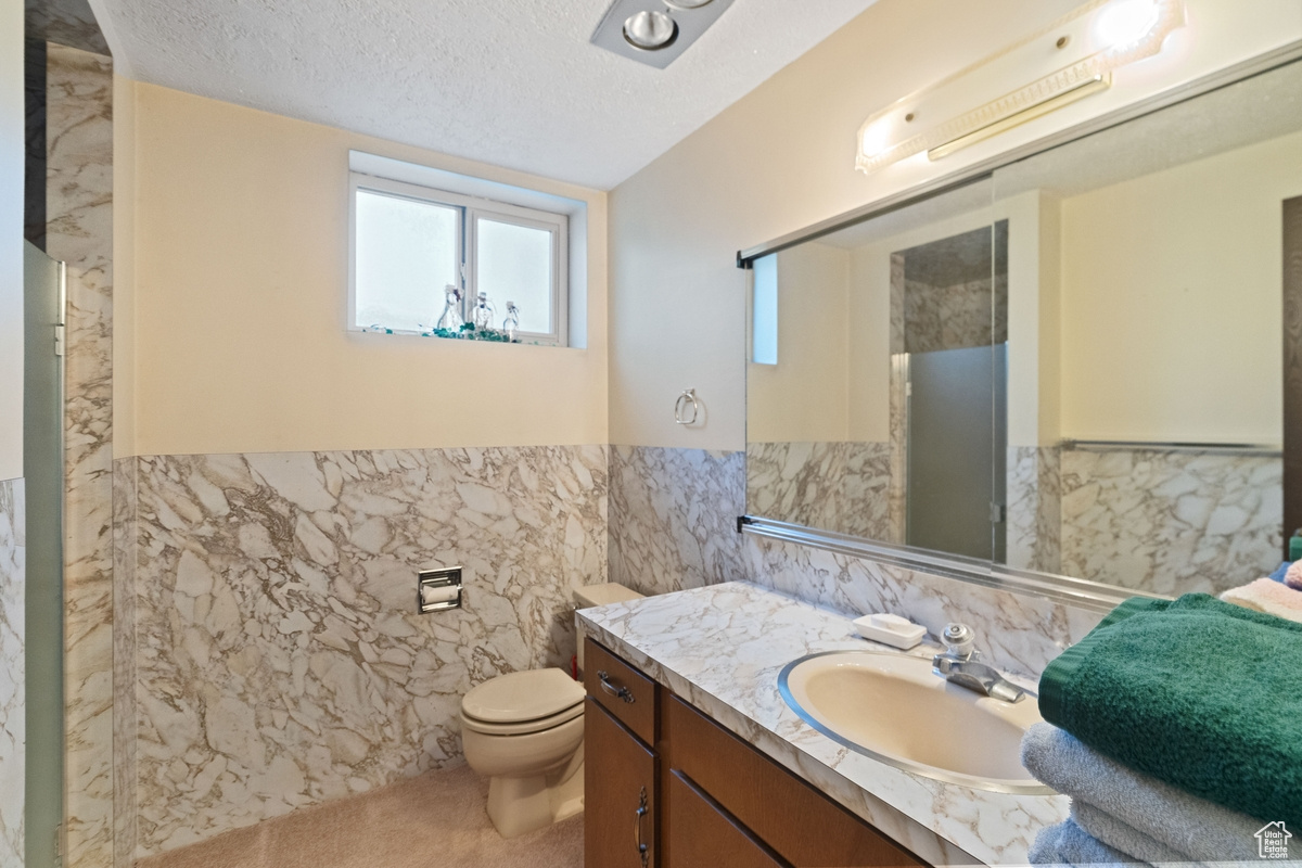 Bathroom with a textured ceiling, tile walls, vanity, and toilet