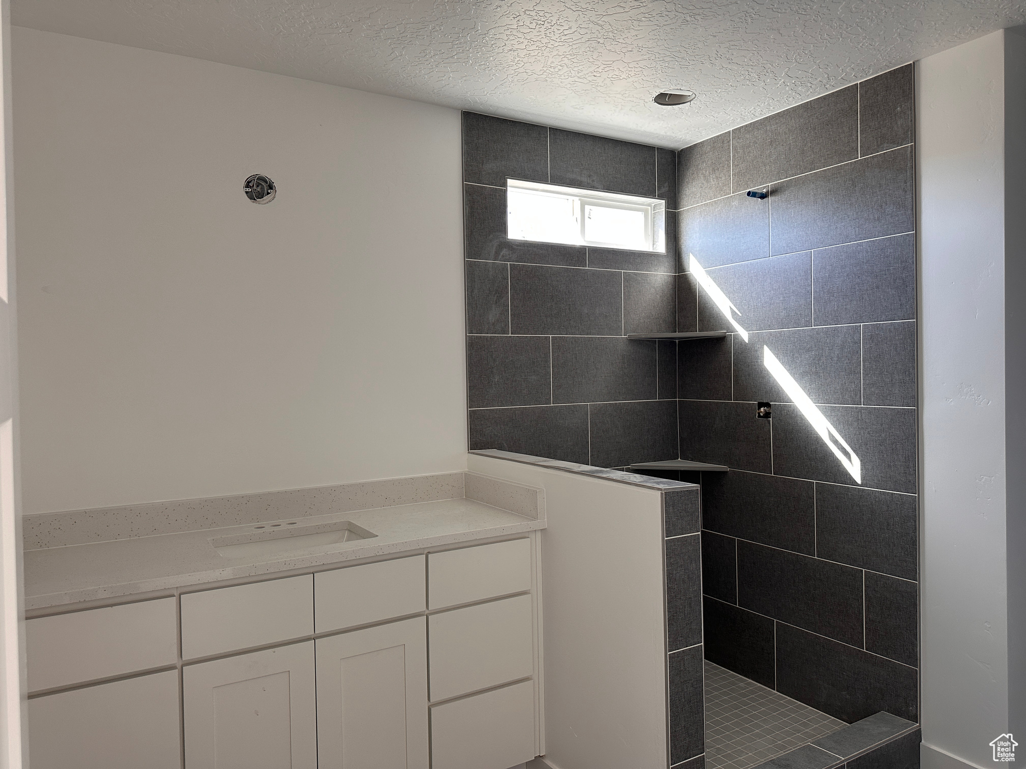 Bathroom with a textured ceiling, vanity, and tiled shower