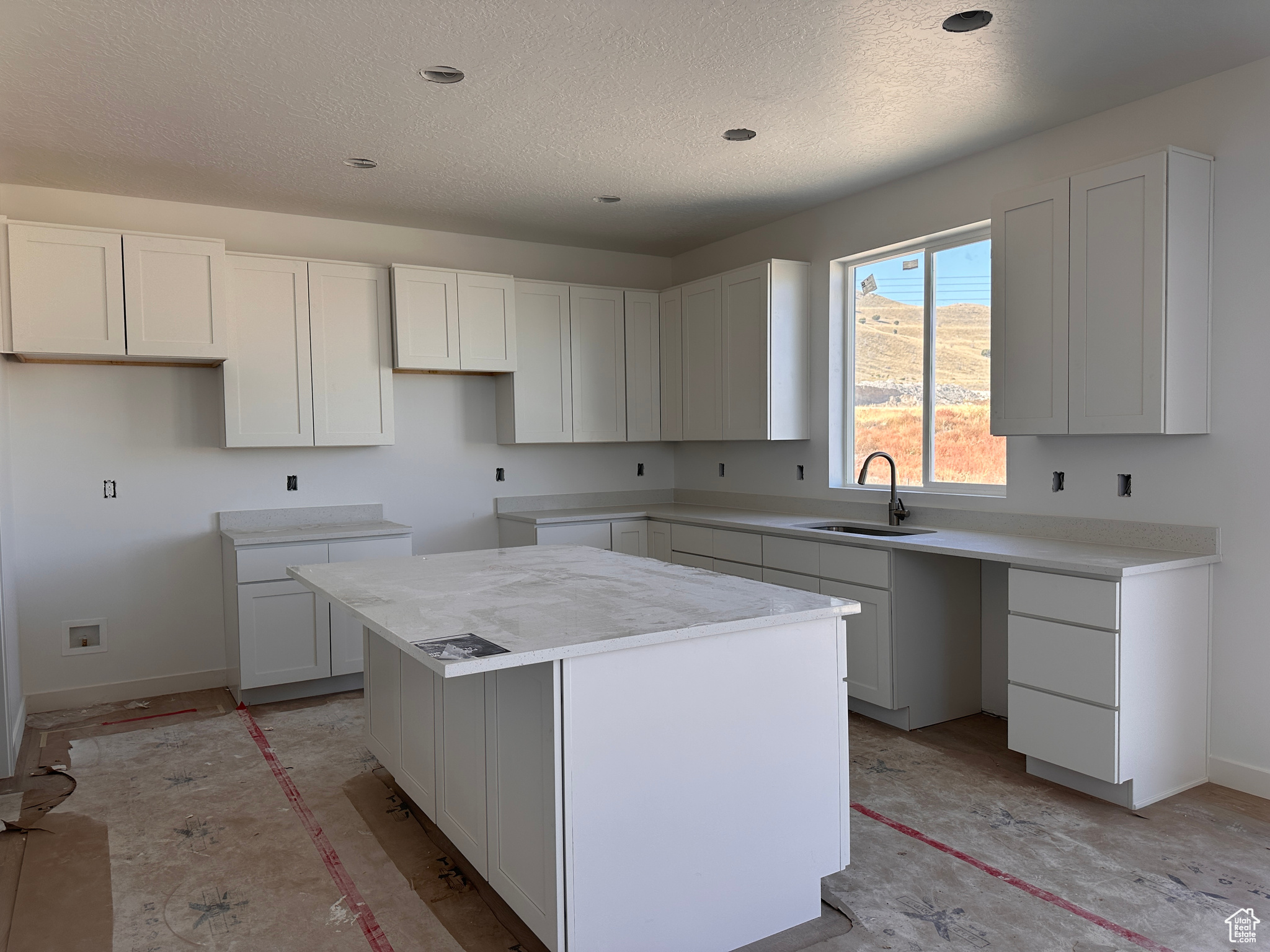 Kitchen with a textured ceiling, a center island, sink, white cabinetry, and light stone countertops