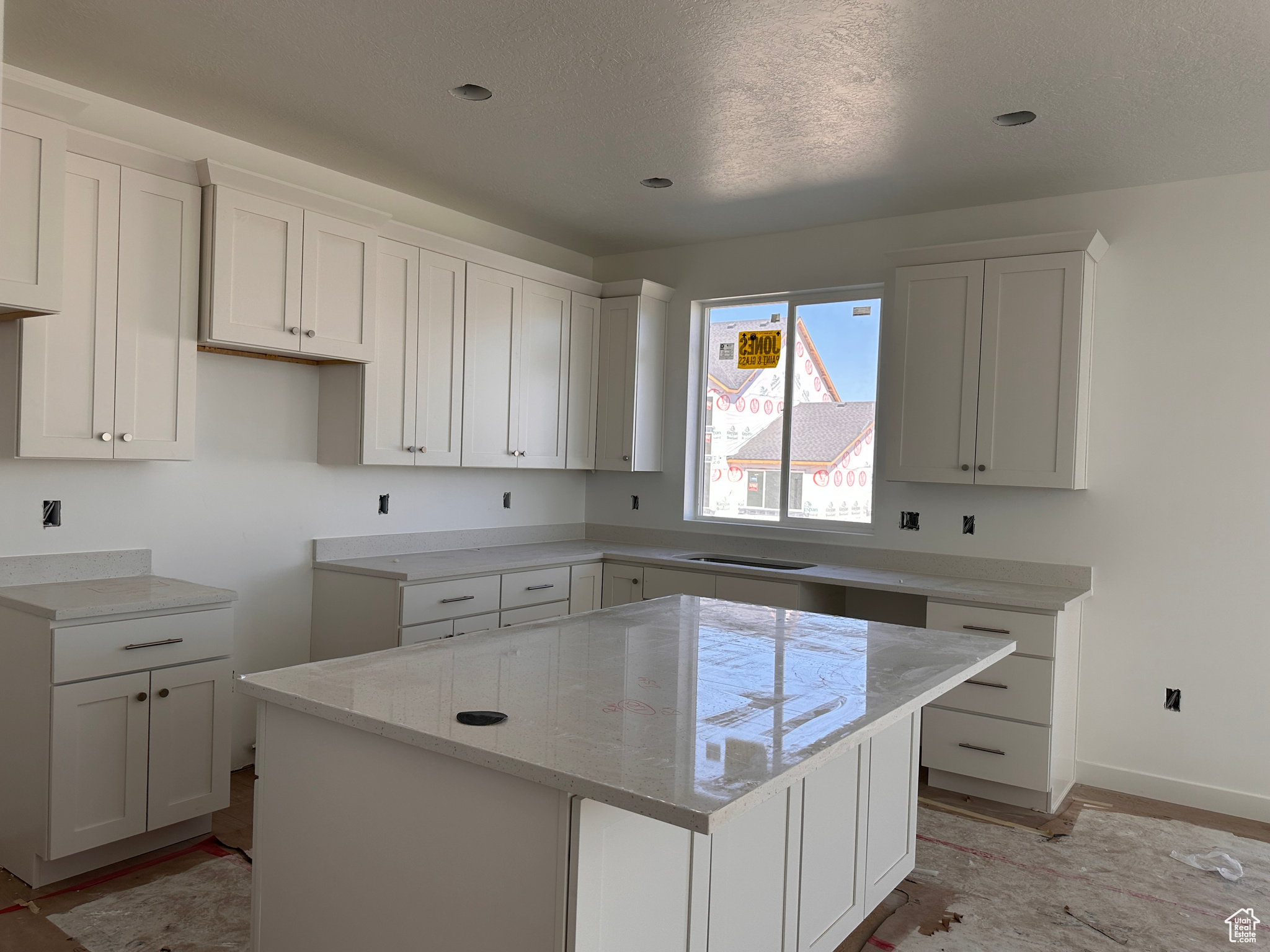 Kitchen with white cabinets, a kitchen island, a textured ceiling, light hardwood / wood-style flooring, and light stone countertops