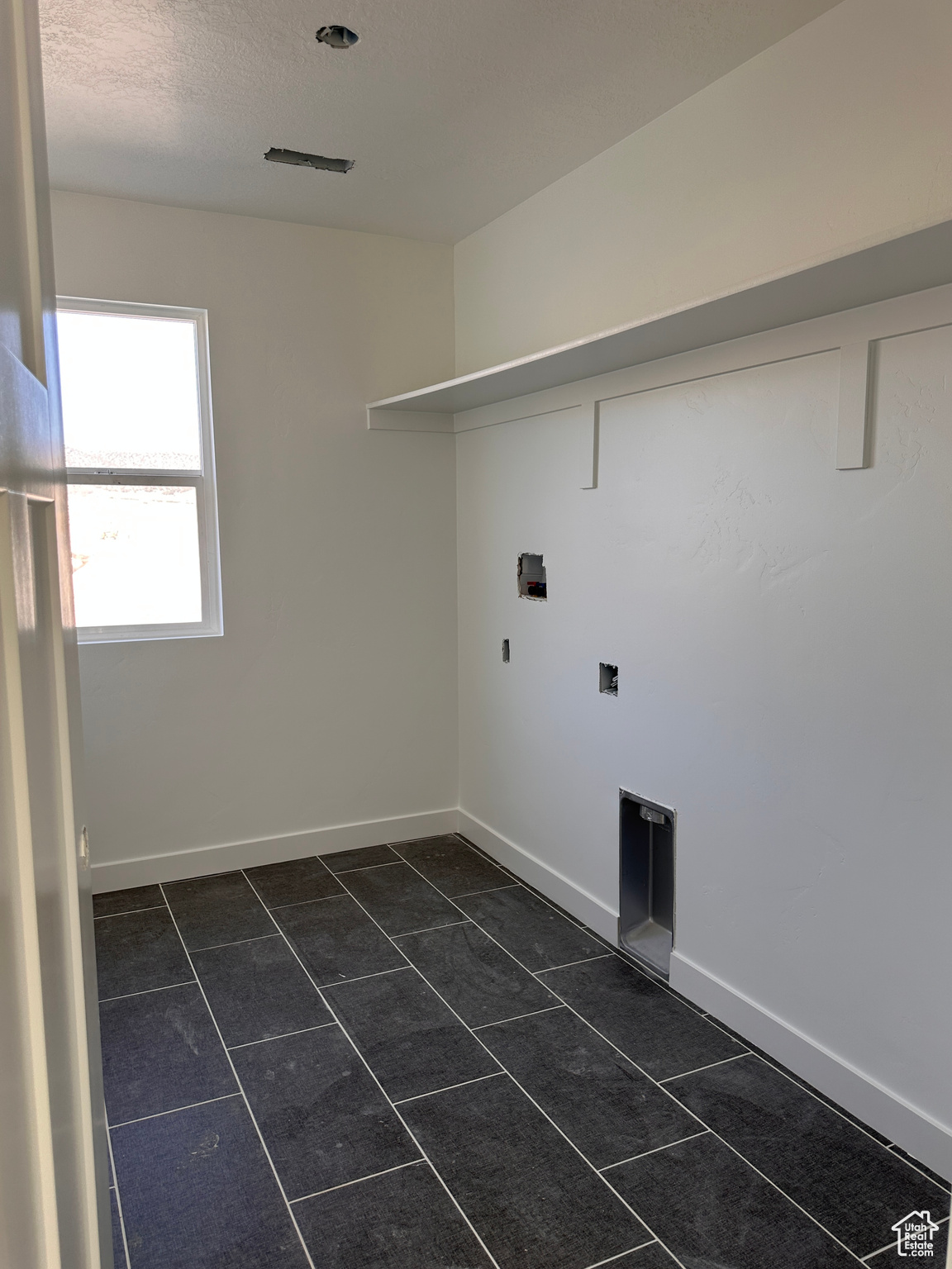 Clothes washing area featuring dark tile patterned flooring, a textured ceiling, and hookup for a washing machine