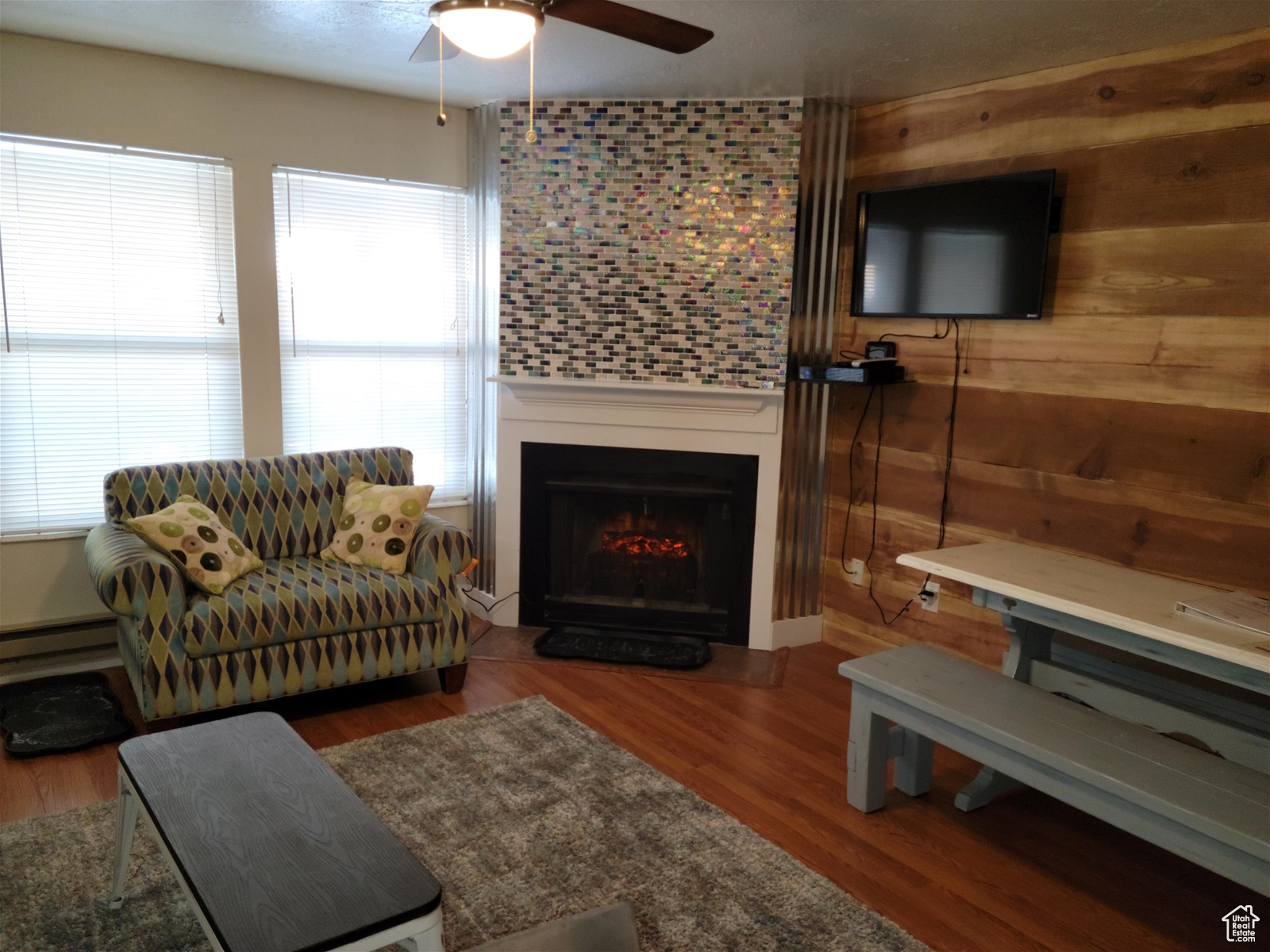 Living room with a fireplace, wood-type flooring, ceiling fan, a baseboard radiator, and wooden walls