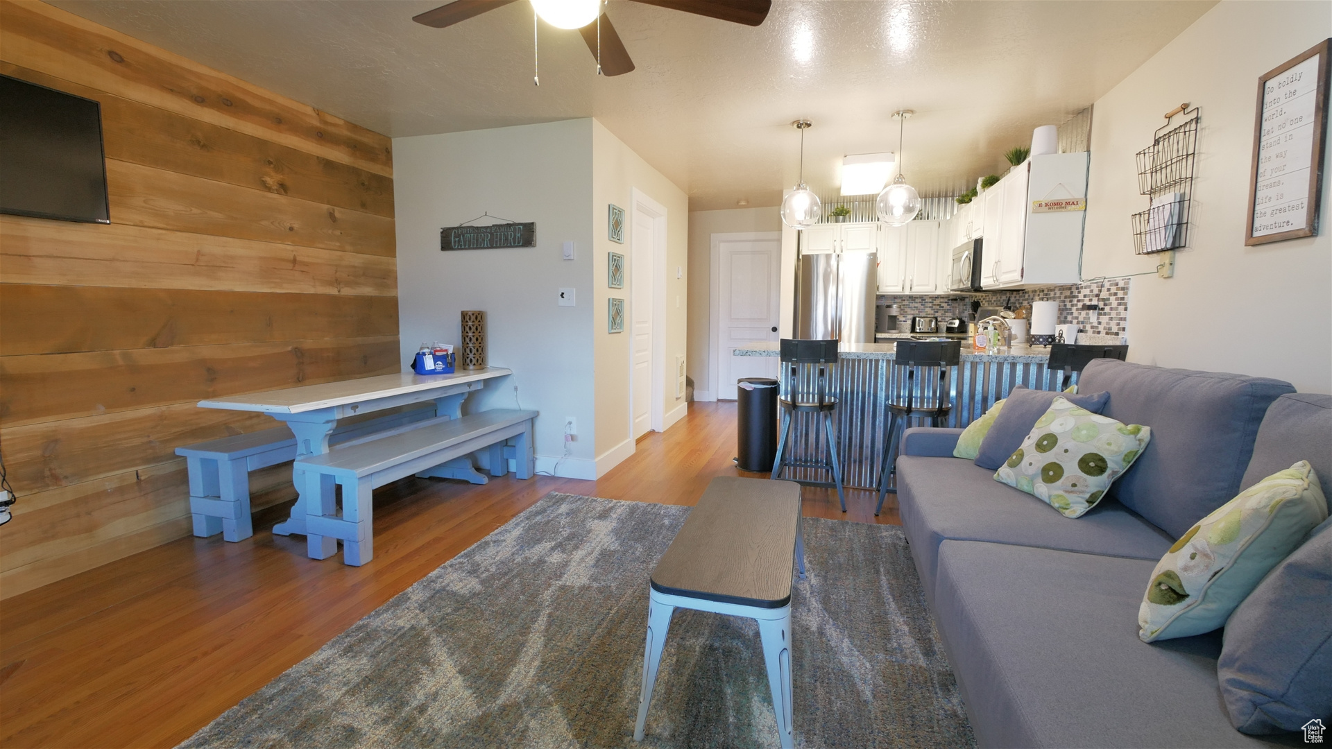 Living room with wooden walls, ceiling fan with notable chandelier, and light wood-type flooring