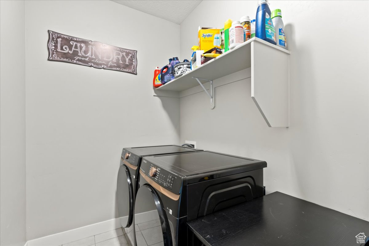 Laundry room with a textured ceiling, light tile patterned flooring, and washing machine and dryer