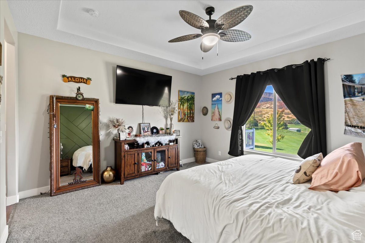 Bedroom featuring a raised ceiling, carpet flooring, and ceiling fan