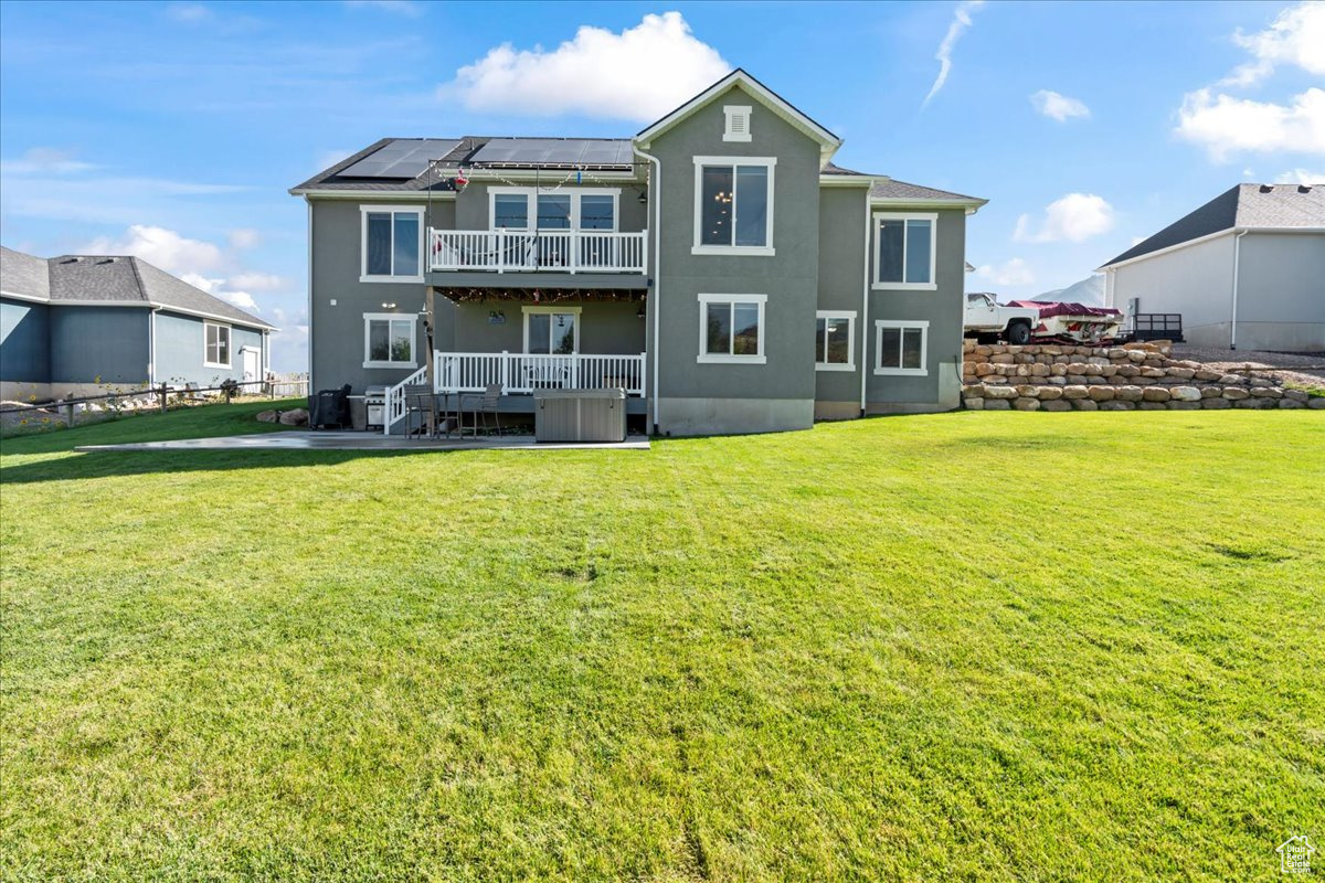 Rear view of house featuring a balcony, solar panels, a wooden deck, a lawn, and cooling unit