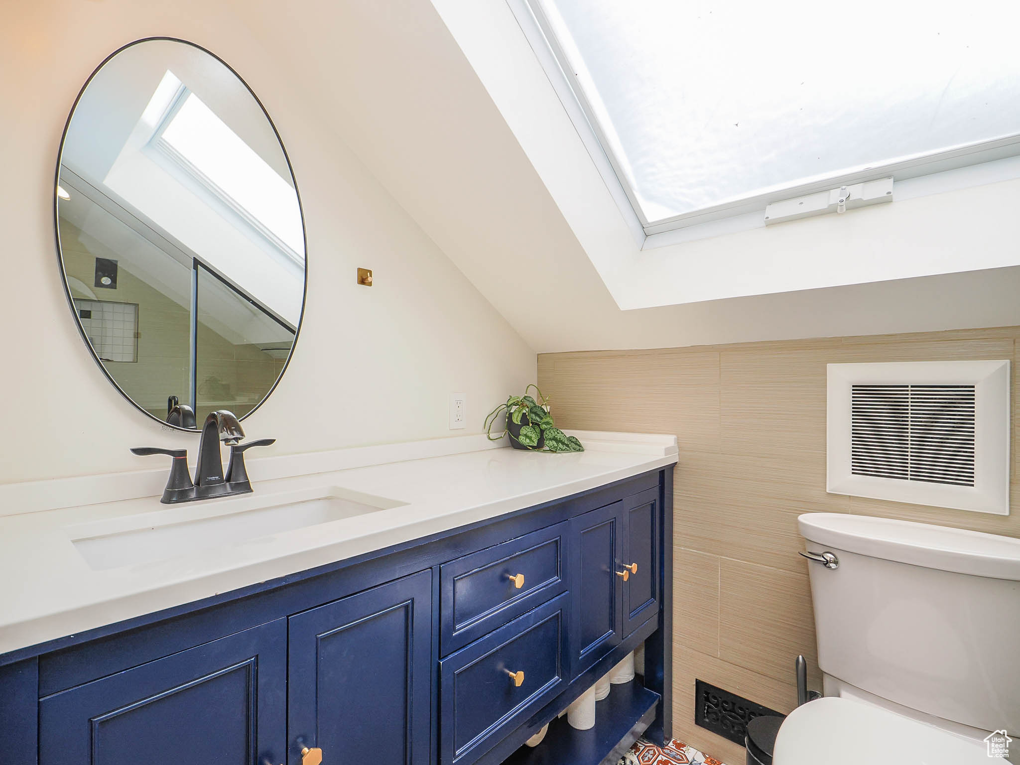 Bathroom with tile walls, vaulted ceiling with skylight, vanity, and toilet