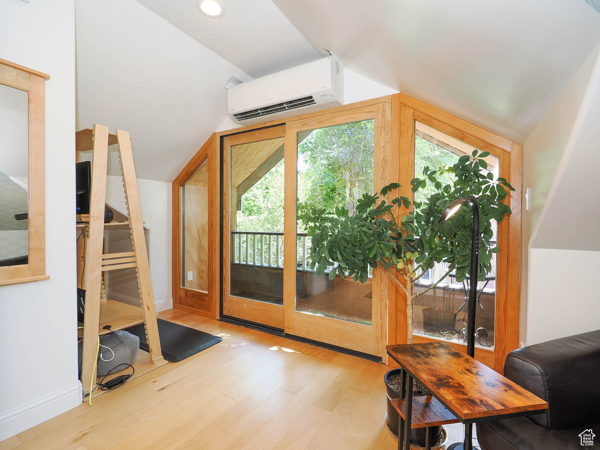 Interior space with light hardwood / wood-style floors, lofted ceiling, and a wall unit AC