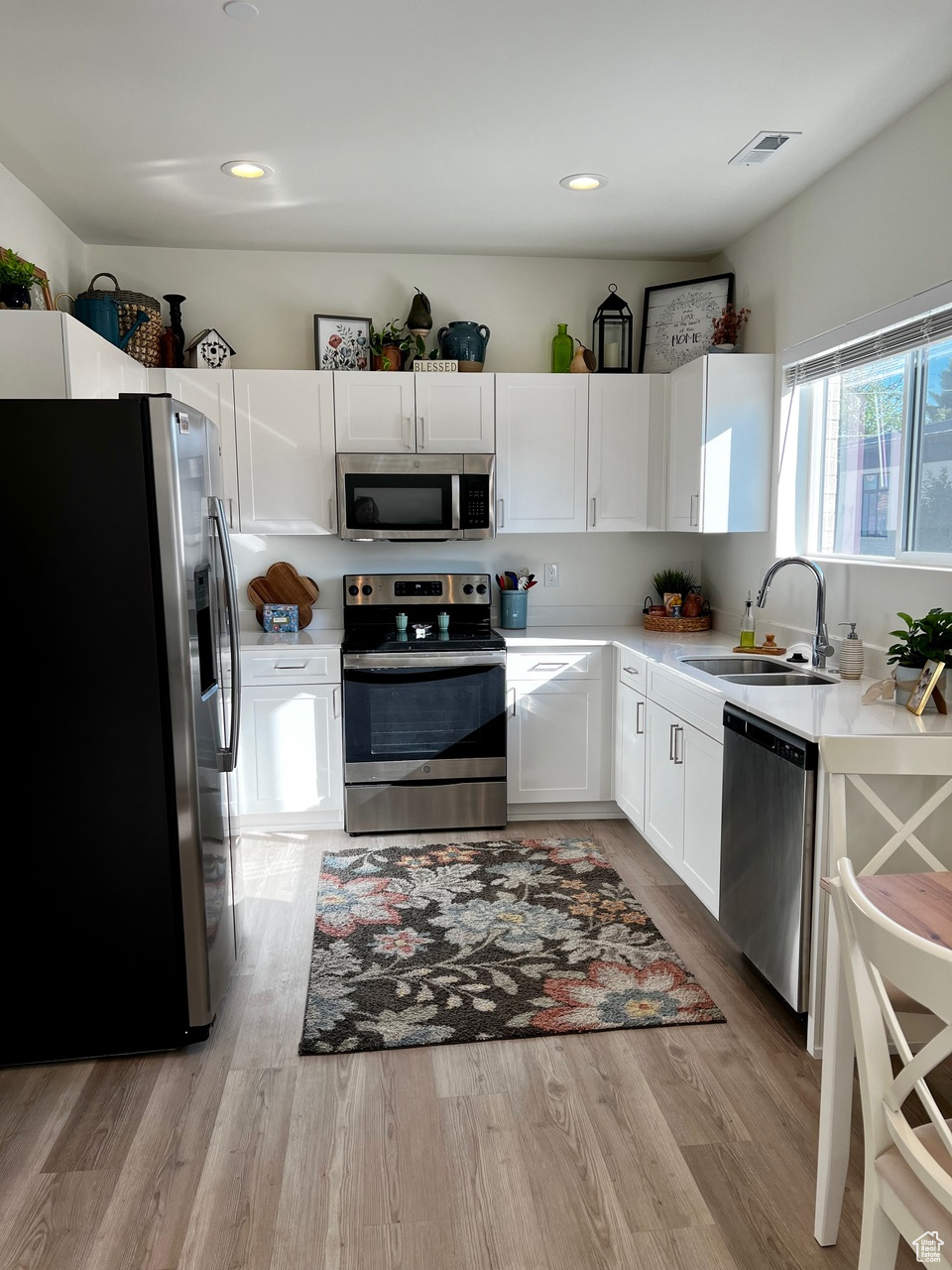 Kitchen featuring stainless steel appliances, white cabinets, light hardwood / wood-style floors, and sink