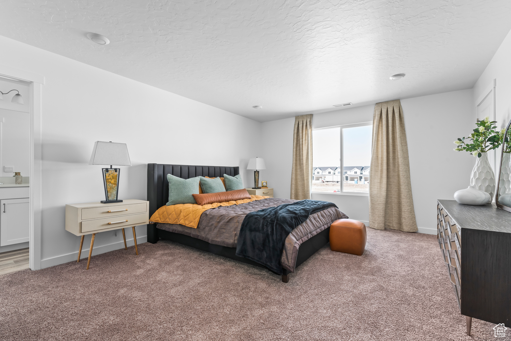 Bedroom featuring a textured ceiling, connected bathroom, and light colored carpet