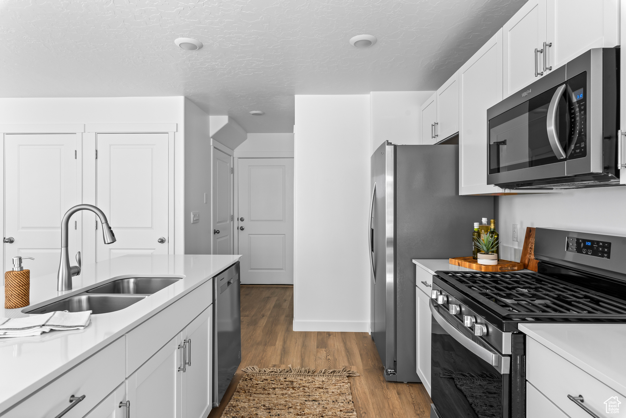 Kitchen featuring white cabinets, sink, wood-type flooring, a textured ceiling, and stainless steel appliances