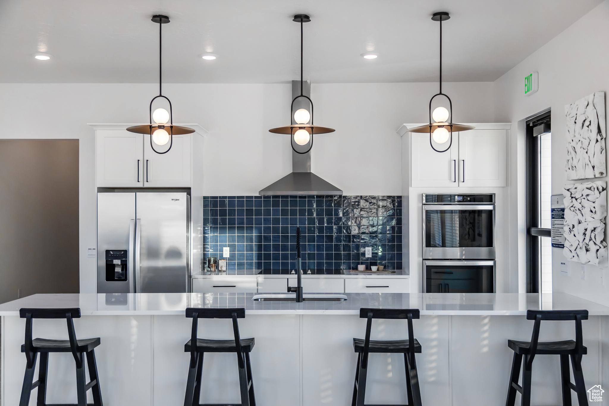 Kitchen with a kitchen breakfast bar, tasteful backsplash, white cabinets, stainless steel appliances, and decorative light fixtures