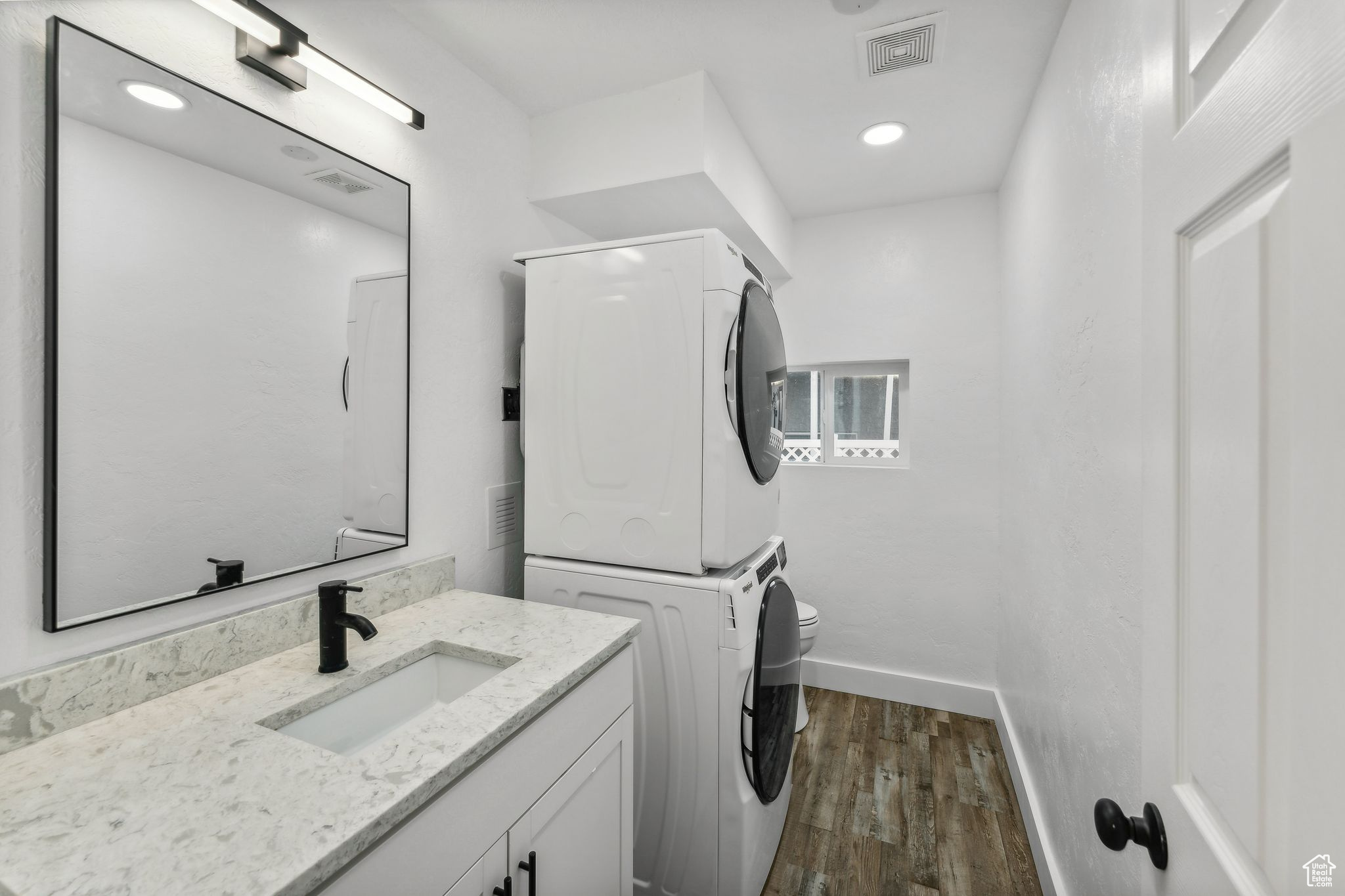 Laundry room with stacked washer / drying machine, sink, and dark hardwood / wood-style flooring