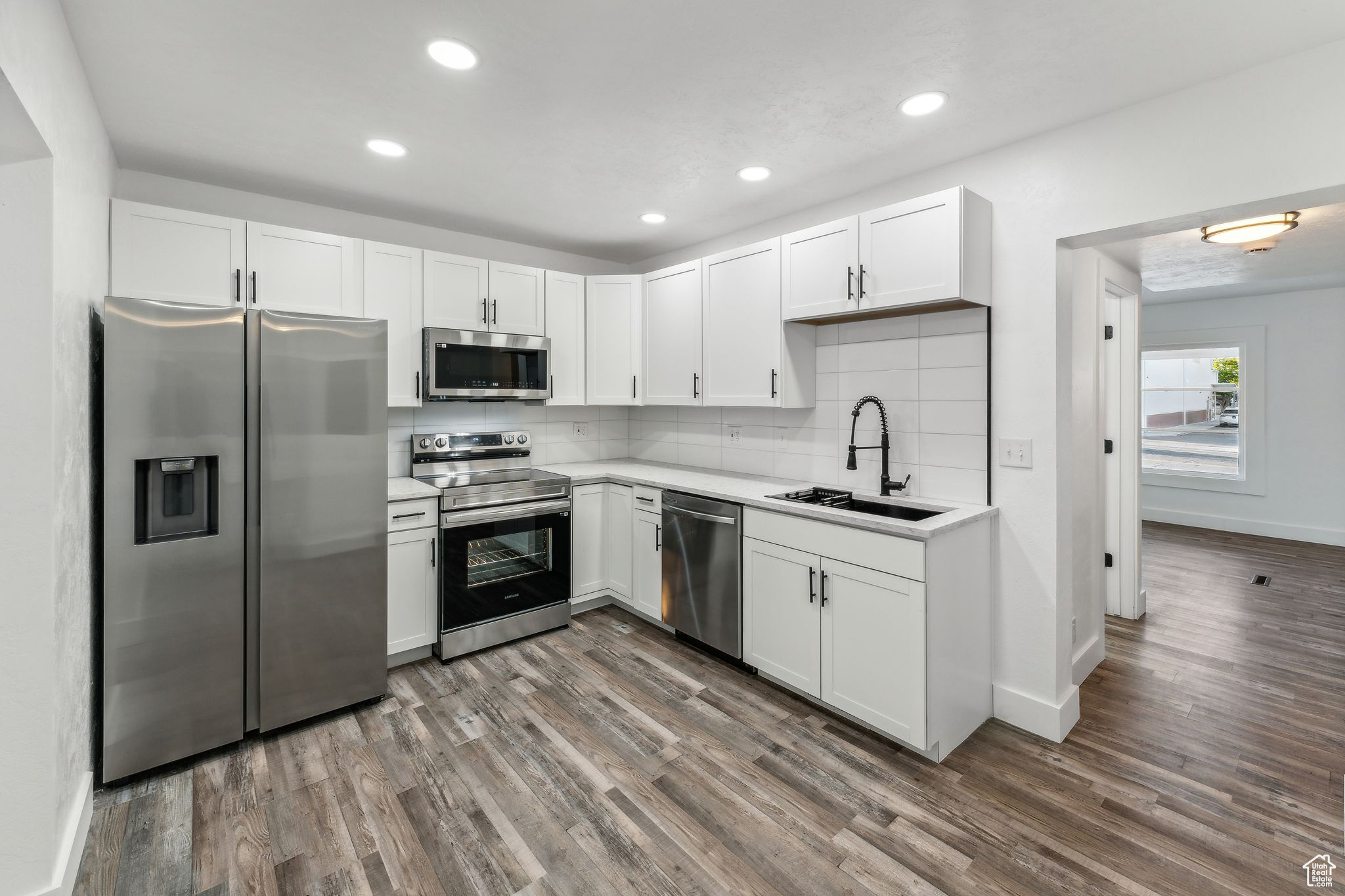 Kitchen with appliances with stainless steel finishes, dark hardwood / wood-style floors, sink, and white cabinetry