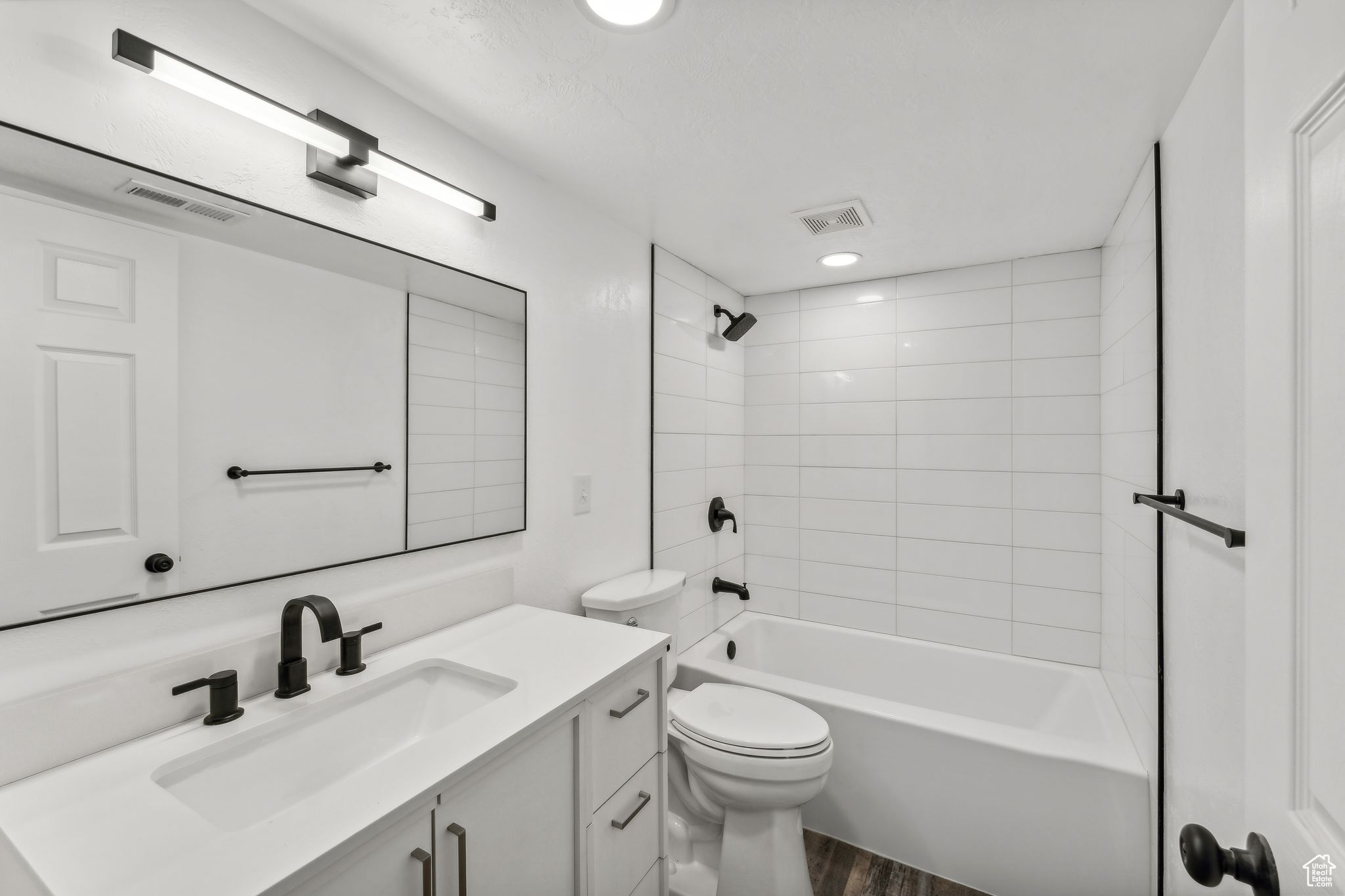 Full bathroom with tiled shower / bath combo, vanity, toilet, and wood-type flooring