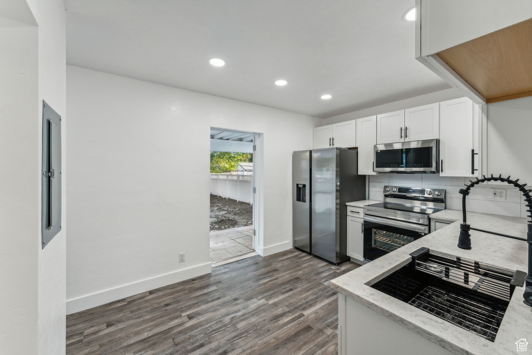 Kitchen with light stone counters, white cabinets, stainless steel appliances, and dark hardwood / wood-style floors