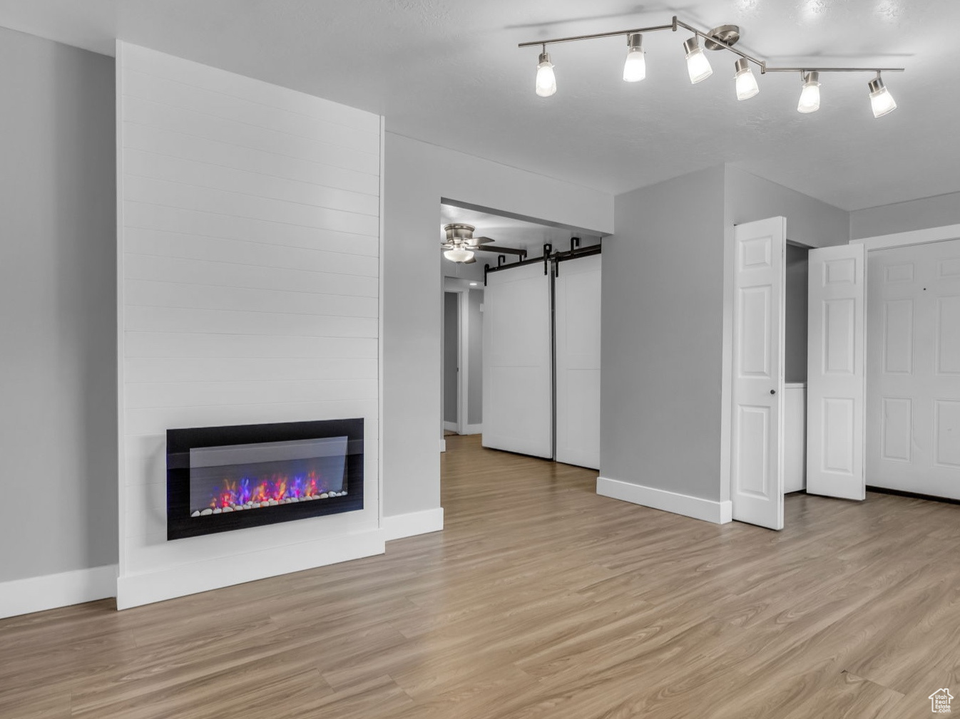 Unfurnished living room with track lighting, a textured ceiling, a barn door, a fireplace, and light hardwood / wood-style floors