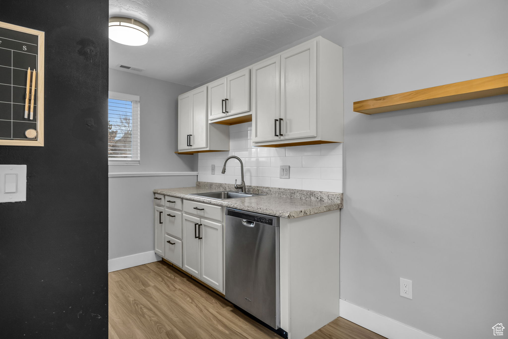 Kitchen with sink, light hardwood / wood-style flooring, stainless steel dishwasher, decorative backsplash, and white cabinets