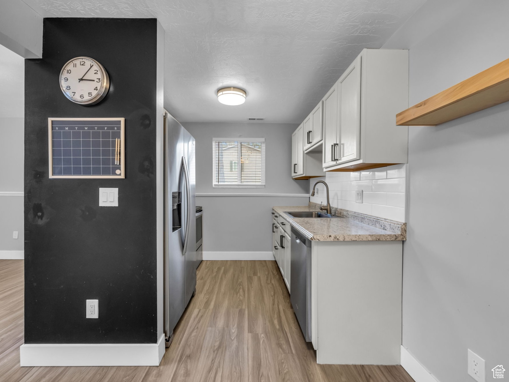 Kitchen with white cabinetry, sink, stainless steel appliances, backsplash, and light hardwood / wood-style floors