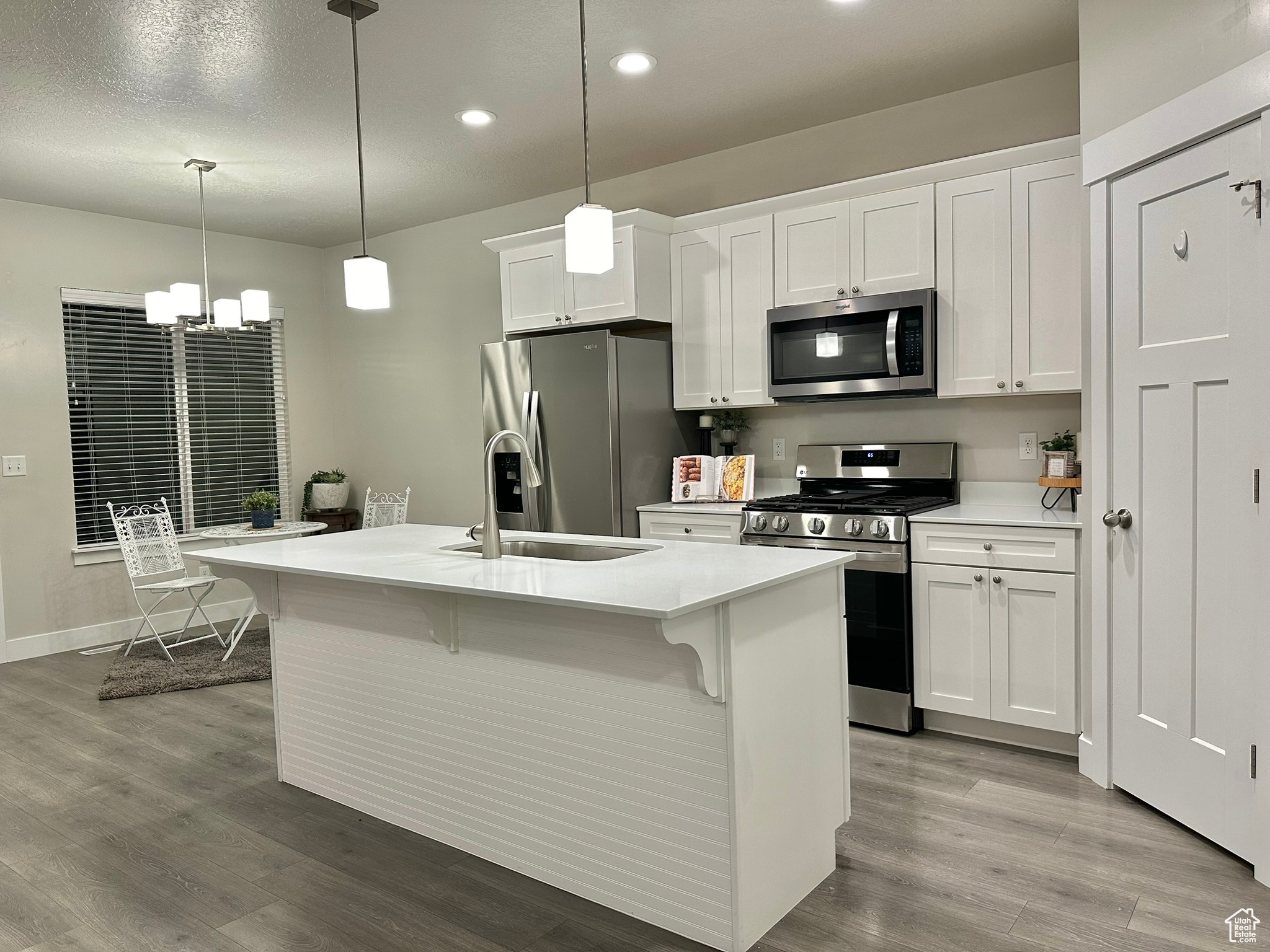 Kitchen featuring light wood-type flooring, an island with sink, white cabinetry, appliances with stainless steel finishes, and decorative light fixtures