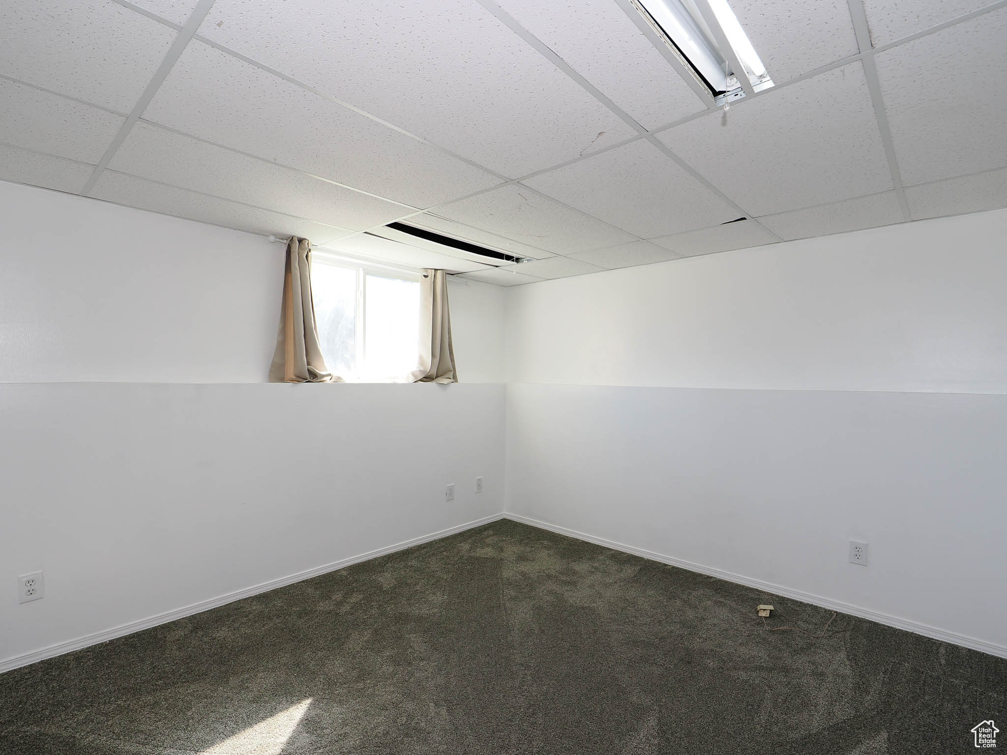 Empty room with a paneled ceiling and dark colored carpet