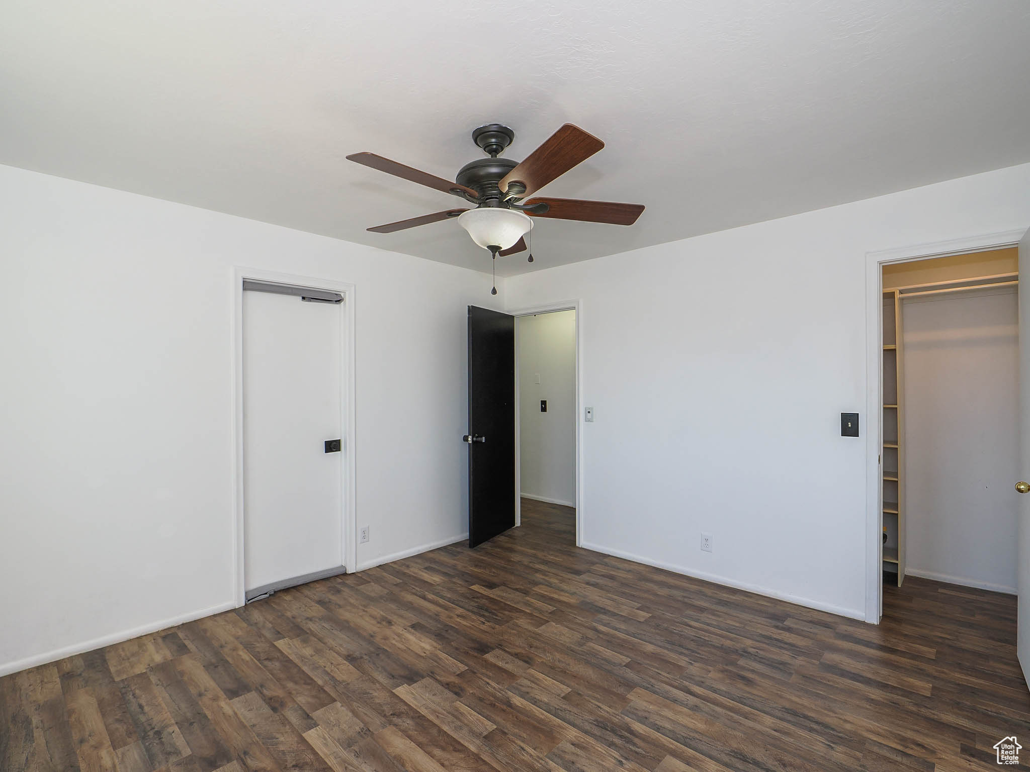 Unfurnished bedroom featuring a spacious closet, ceiling fan, and dark hardwood / wood-style flooring