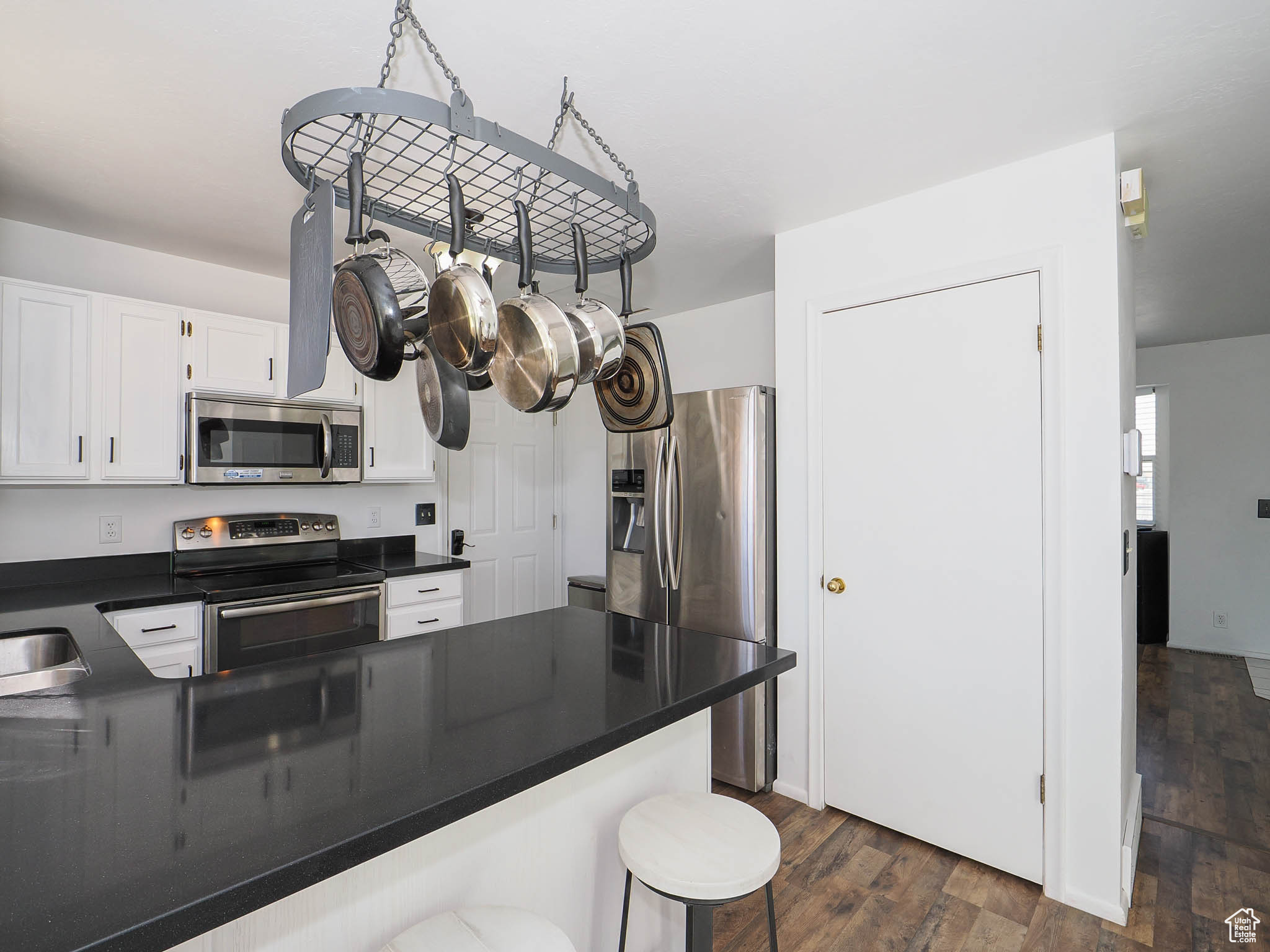 Kitchen with dark hardwood / wood-style floors, sink, white cabinets, a kitchen bar, and stainless steel appliances