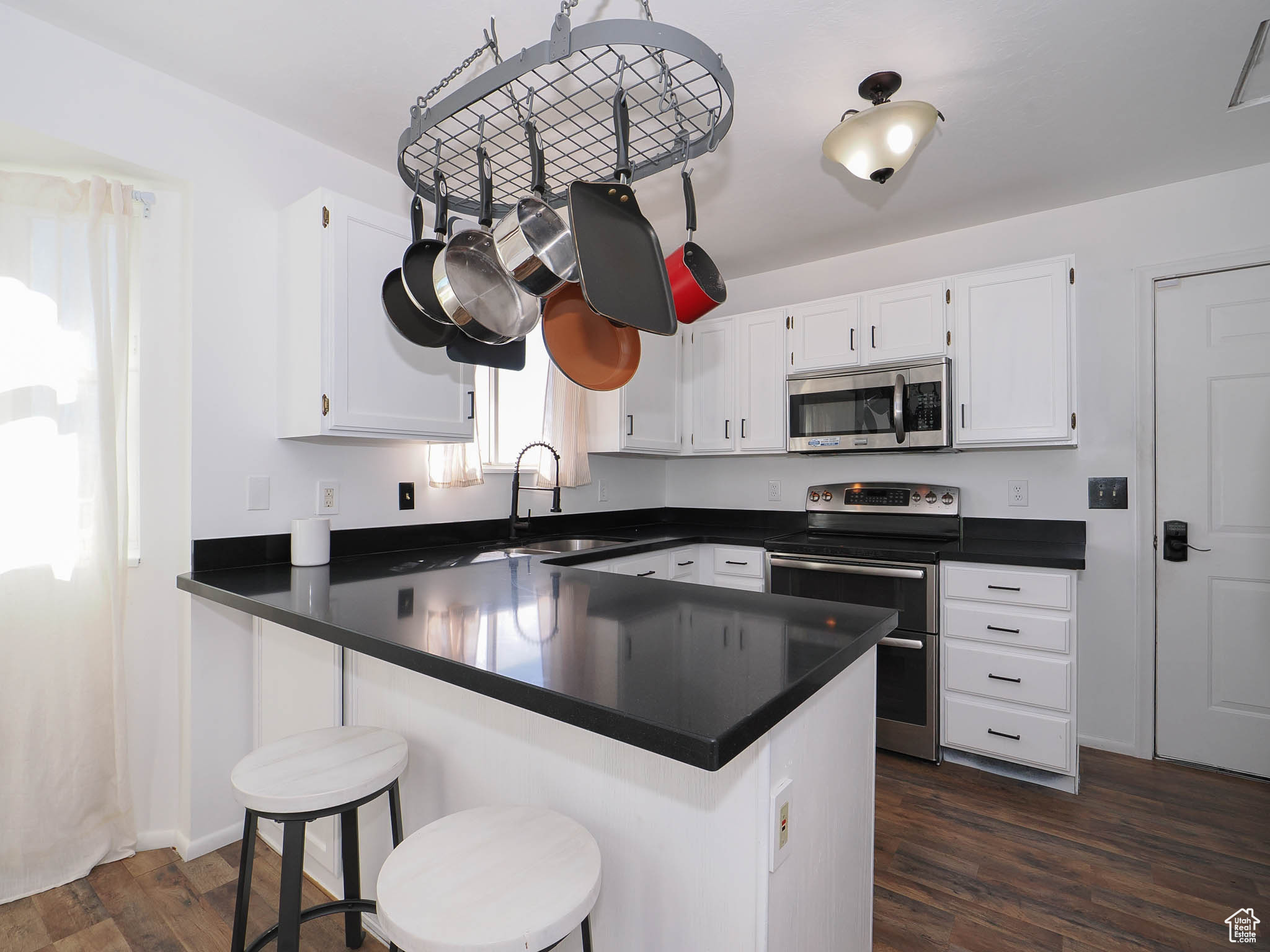 Kitchen with kitchen peninsula, dark hardwood / wood-style floors, stainless steel appliances, and white cabinets