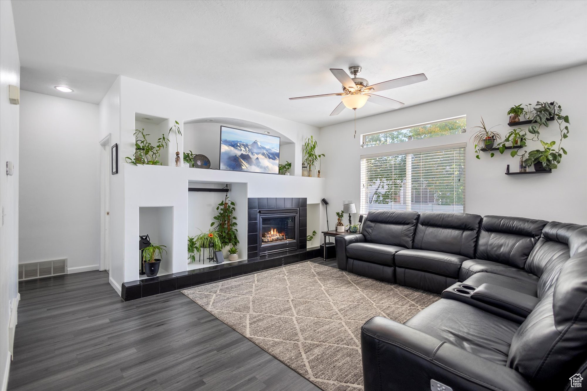 Living room with a fireplace, ceiling fan, and dark wood-type flooring