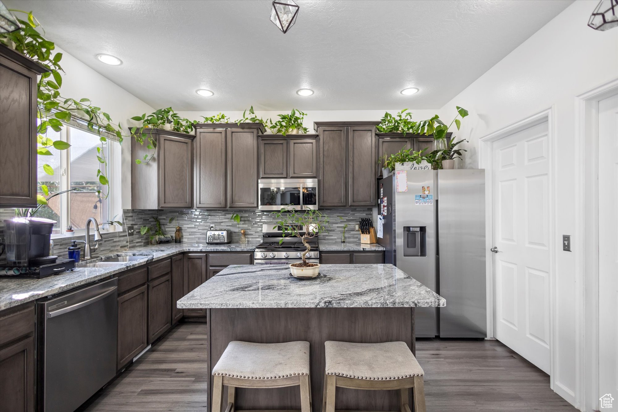 Kitchen with appliances with stainless steel finishes, light stone counters, a kitchen island, dark hardwood / wood-style flooring, and sink