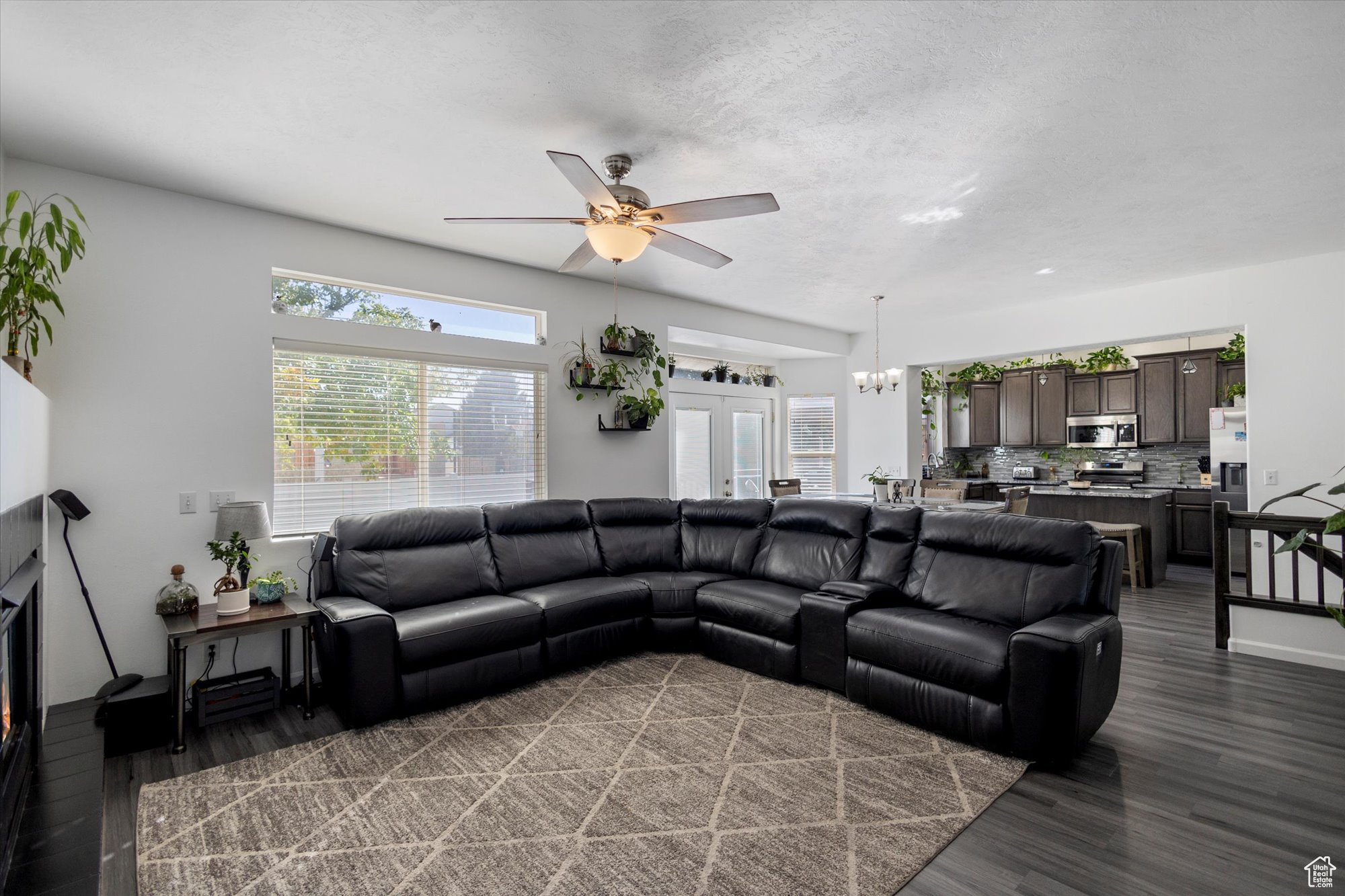 Living room featuring a textured ceiling, ceiling fan with notable chandelier, and dark wood-type flooring