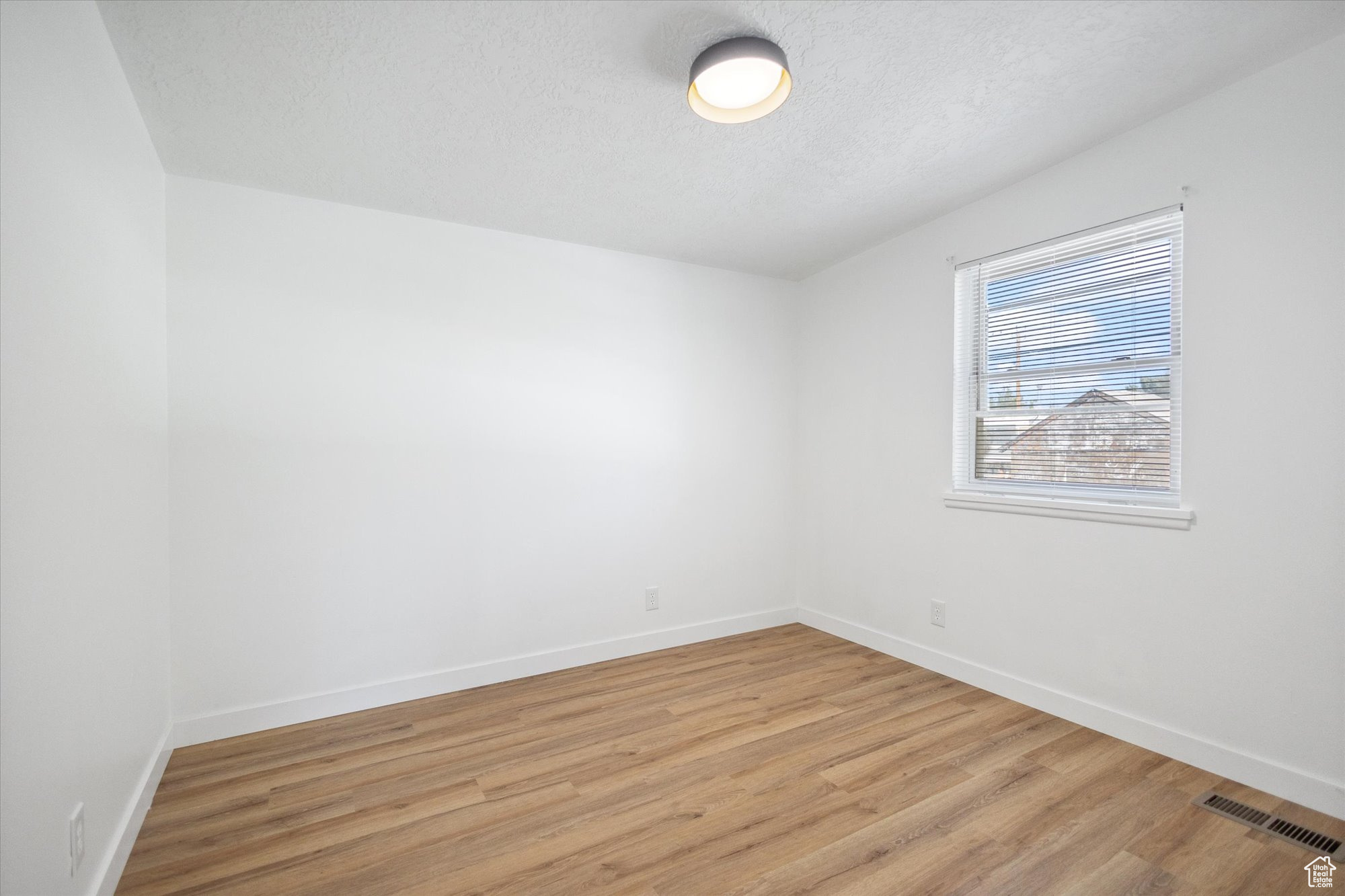 Spare room with a textured ceiling and light hardwood / wood-style floors