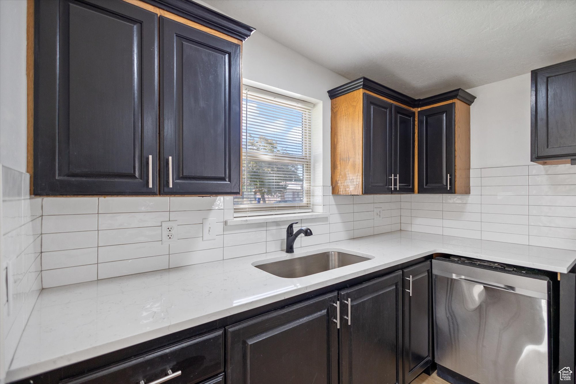 Kitchen featuring light stone counters, sink, decorative backsplash, and stainless steel dishwasher