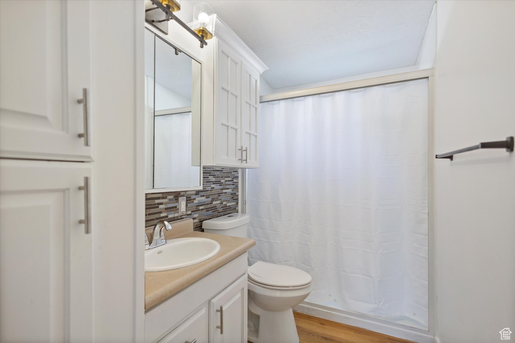 Bathroom with vanity, tasteful backsplash, wood-type flooring, toilet, and a shower with shower curtain