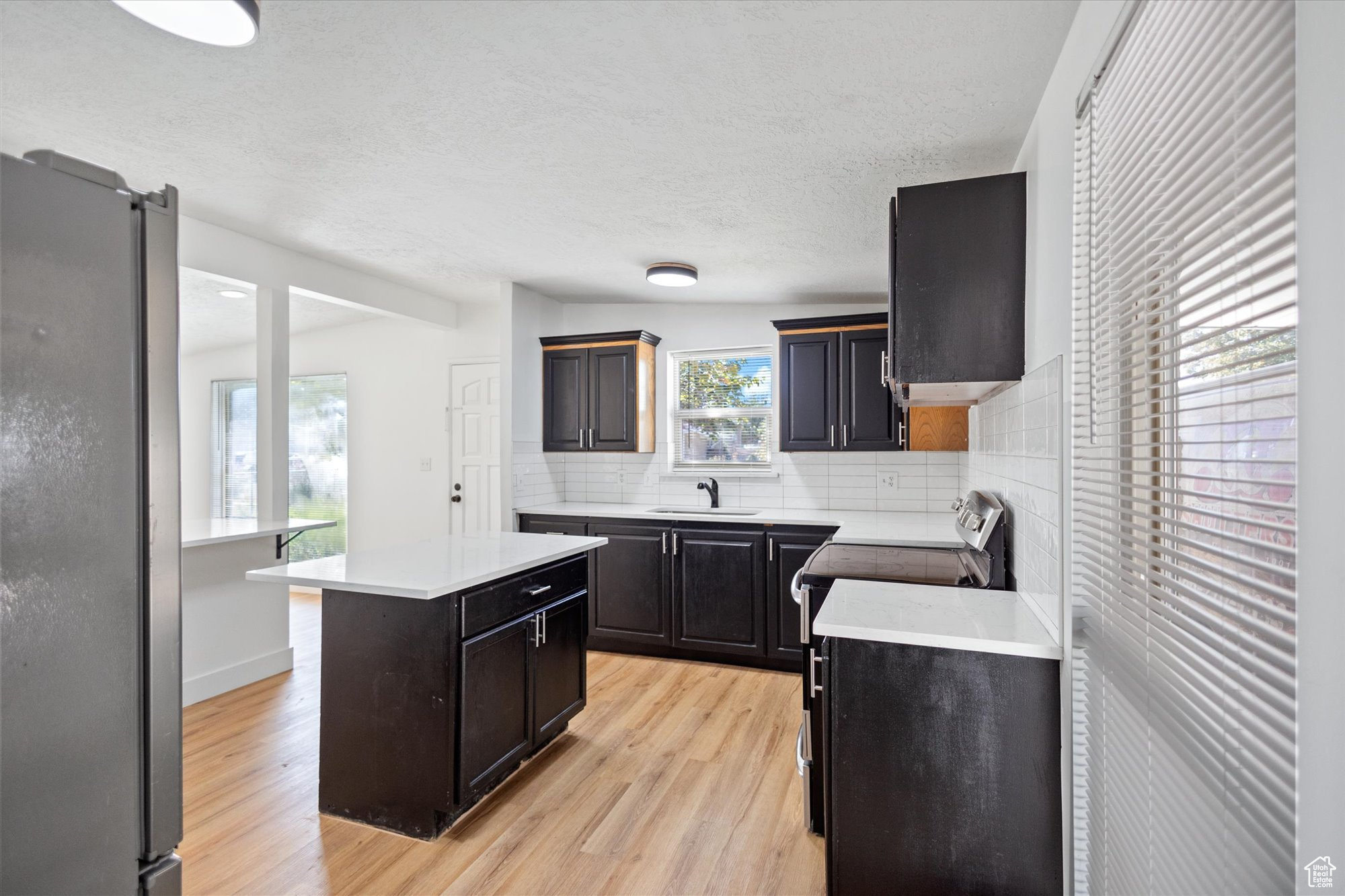 Kitchen with sink, a kitchen island, light hardwood / wood-style flooring, backsplash, and appliances with stainless steel finishes