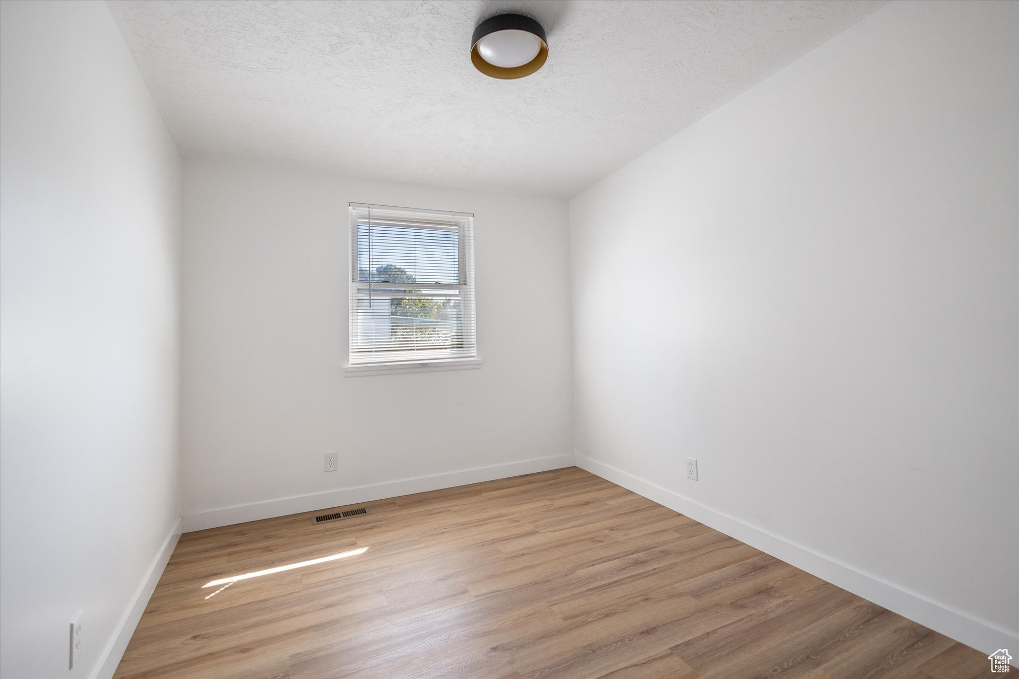 Empty room with light wood-type flooring and a textured ceiling