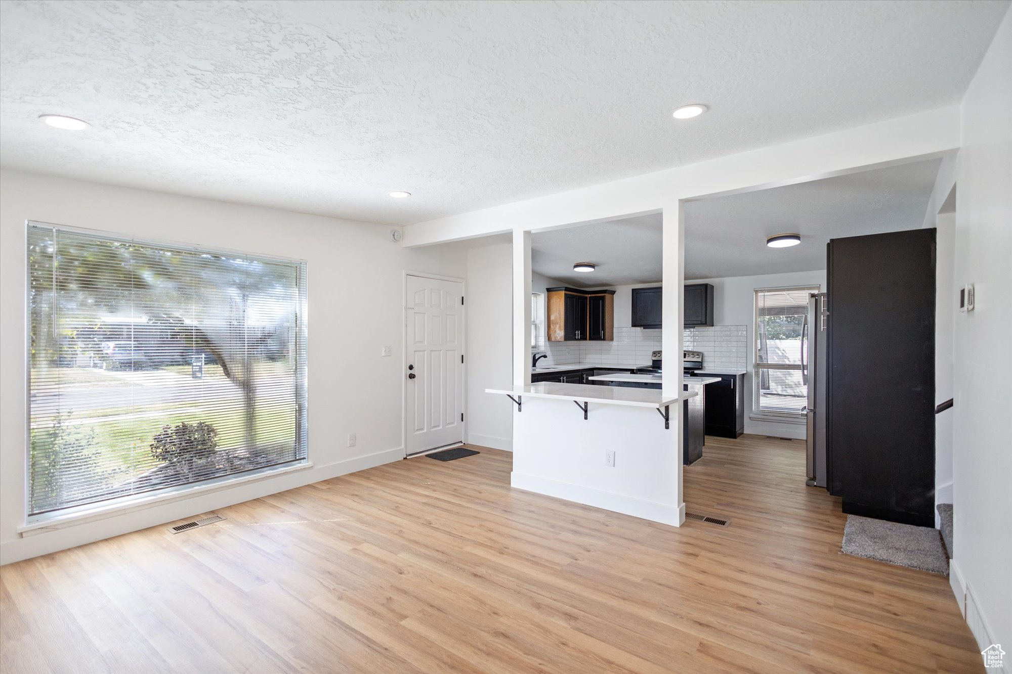 Kitchen featuring decorative backsplash, light hardwood / wood-style floors, a kitchen bar, and stainless steel fridge