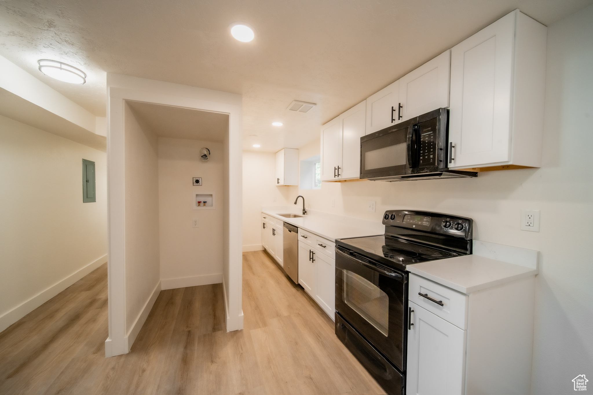 Kitchen featuring white cabinets, sink, light hardwood / wood-style flooring, and black appliances