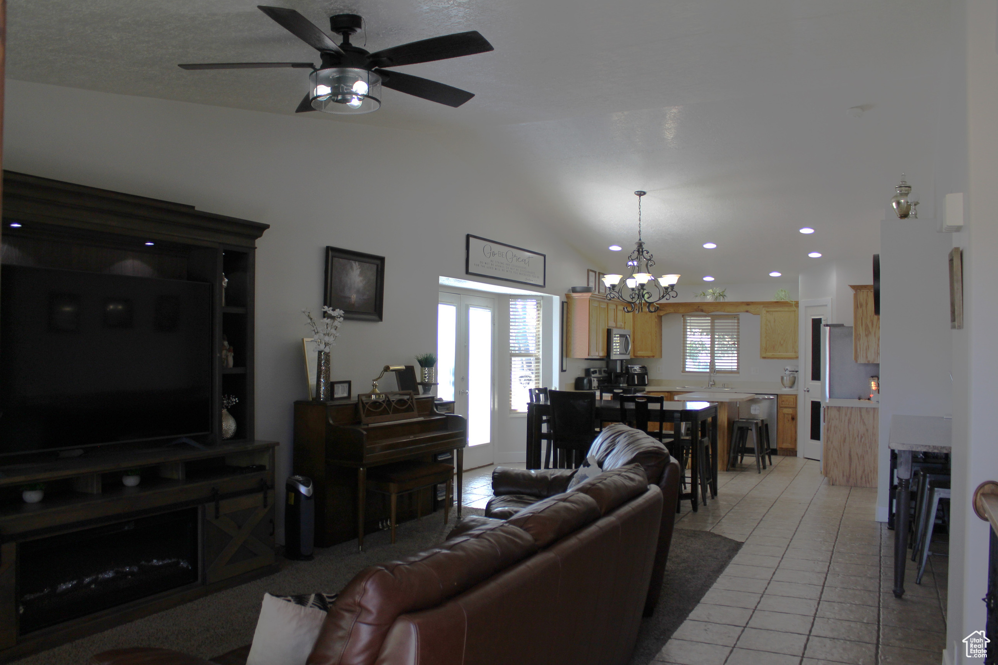 Living room with lofted ceiling, light tile patterned flooring, and ceiling fan with notable chandelier