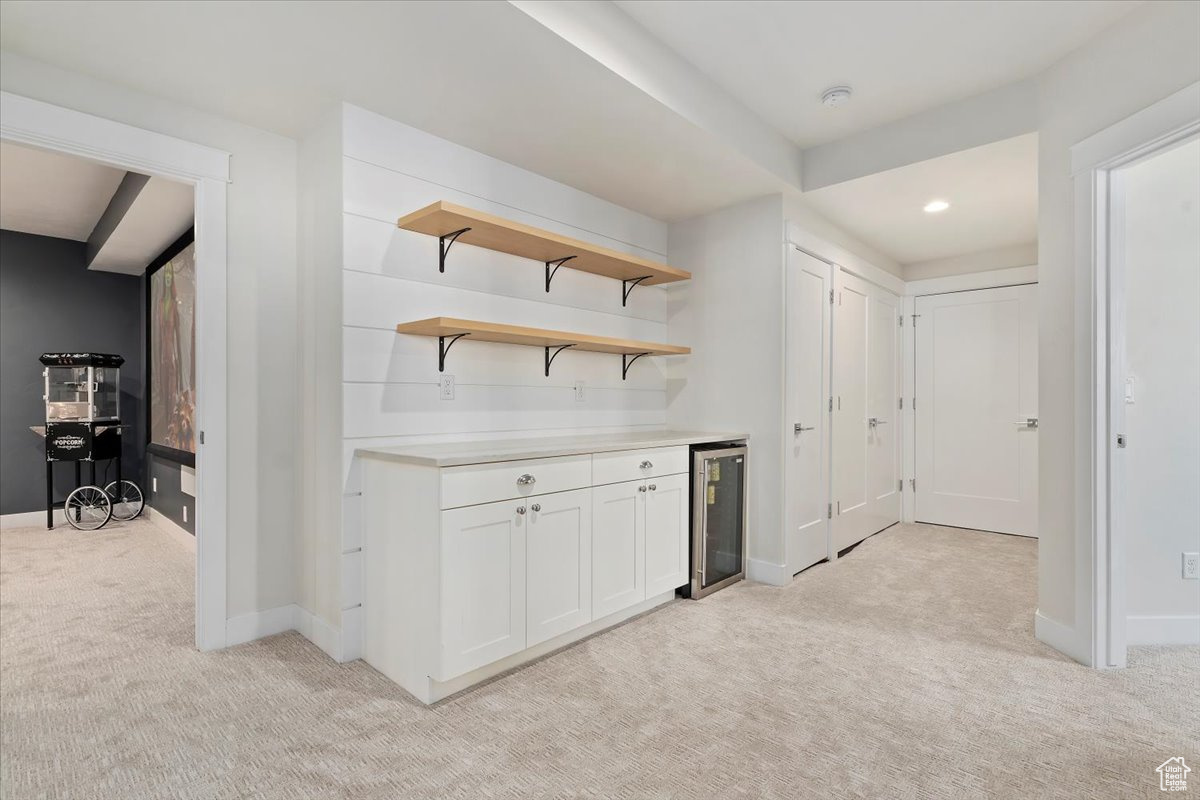 Bar with light carpet, beverage cooler, and white cabinetry