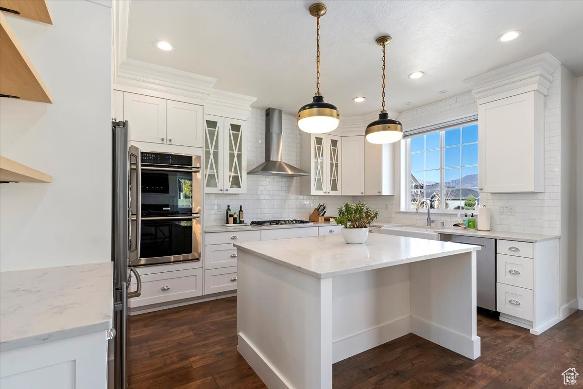 Kitchen with white cabinets, appliances with stainless steel finishes, dark hardwood / wood-style flooring, and wall chimney range hood