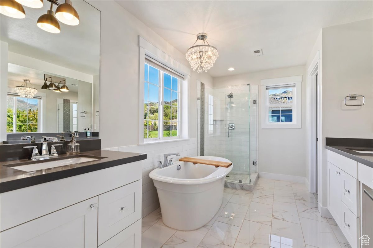 Bathroom featuring independent shower and bath, vanity, tile walls, and a notable chandelier