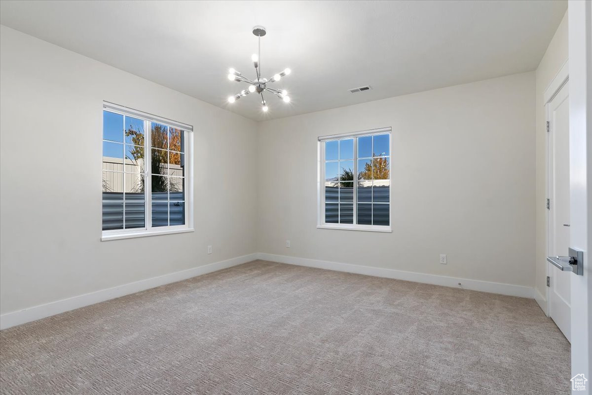 Carpeted empty room featuring a chandelier and plenty of natural light