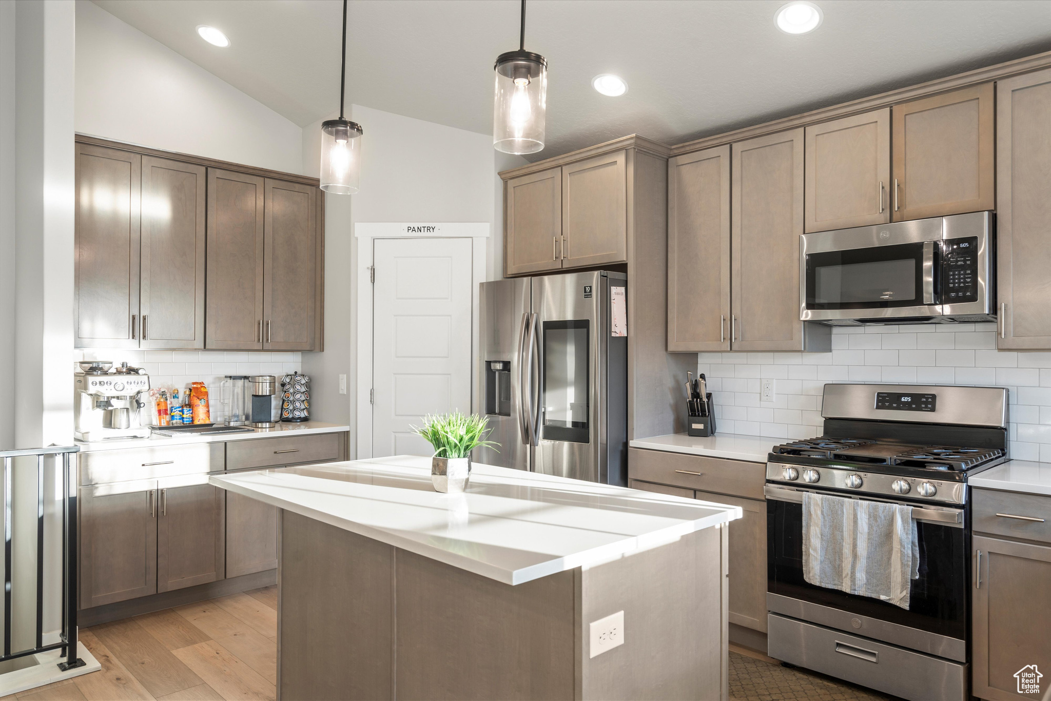 Kitchen featuring light hardwood / wood-style floors, vaulted ceiling, backsplash, stainless steel appliances, and decorative light fixtures