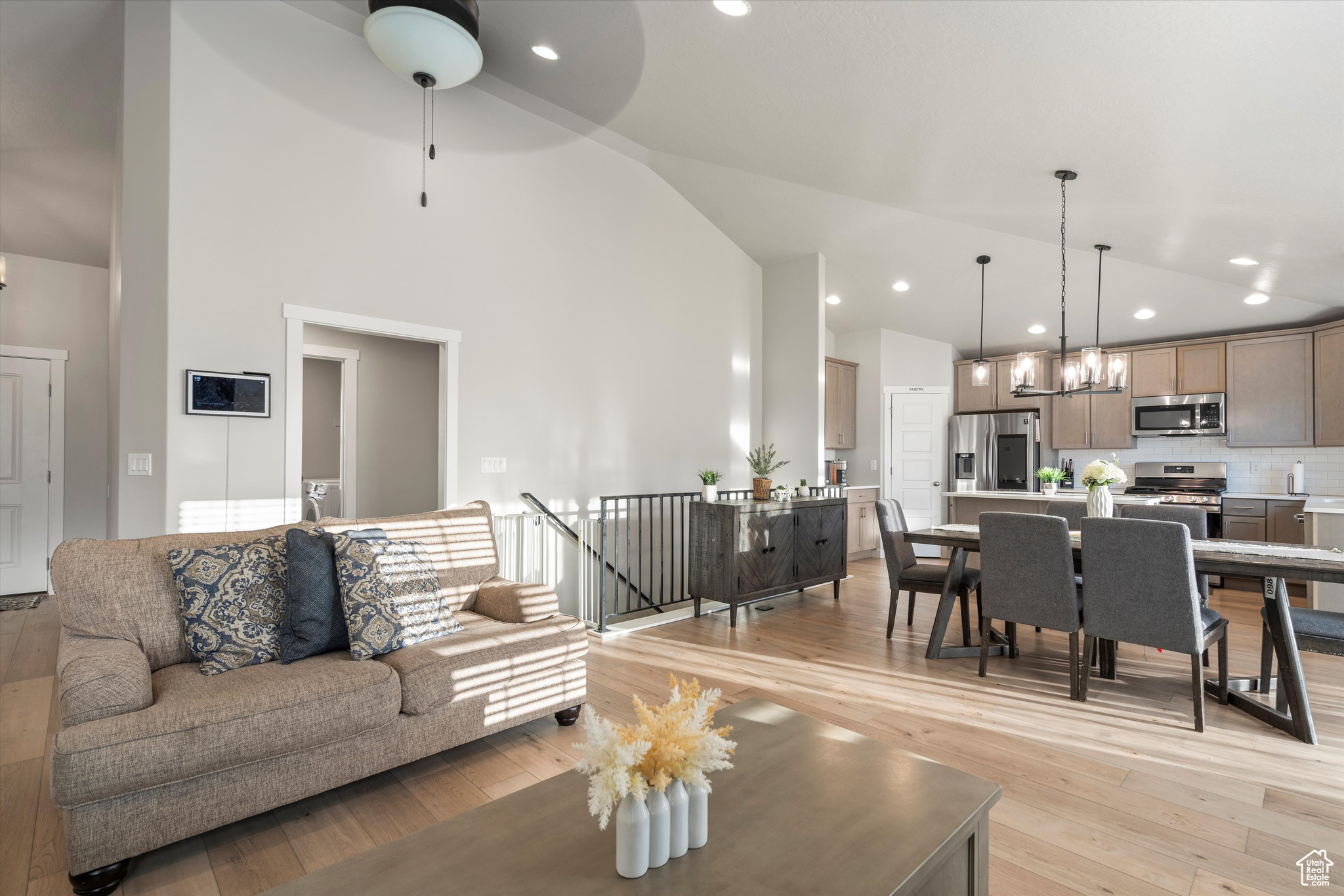 Living room featuring light wood-type flooring, ceiling fan with notable chandelier, and high vaulted ceiling